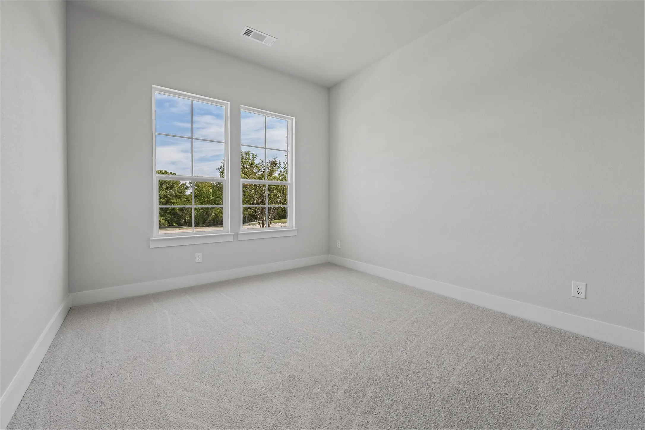 Two large windows, light gray carpeting, and white baseboards