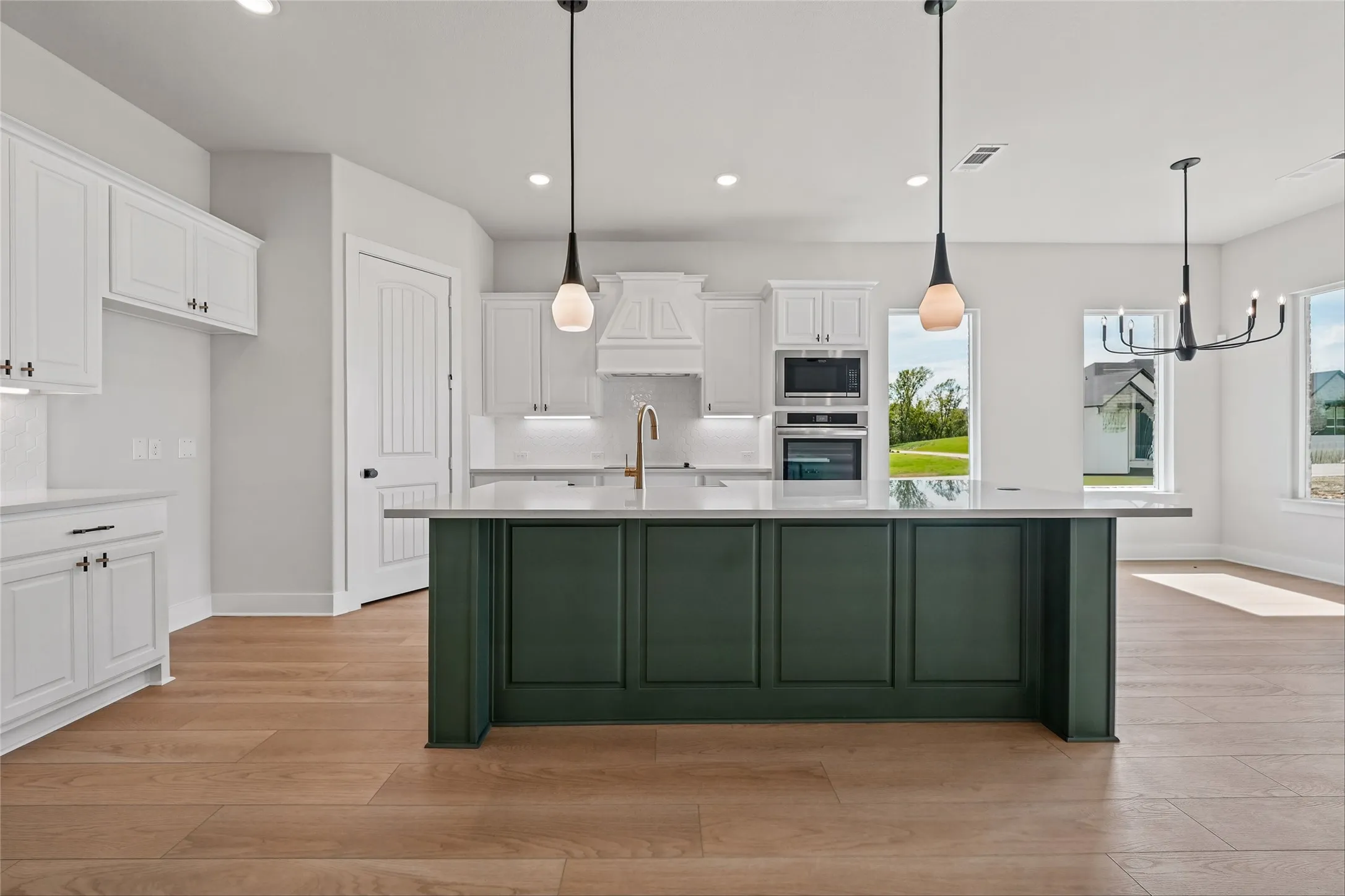 Spacious kitchen featuring a dark green island, white cabinetry, integrated stainless steel appliances, and wood-finish flooring