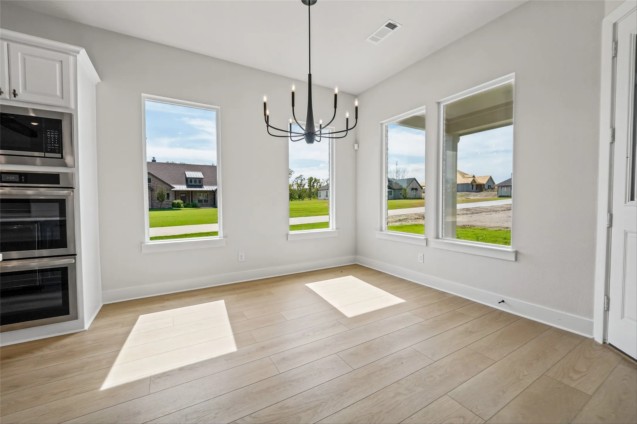Open concept area featuring wood-finish flooring, multiple large windows, and a contemporary chandelier