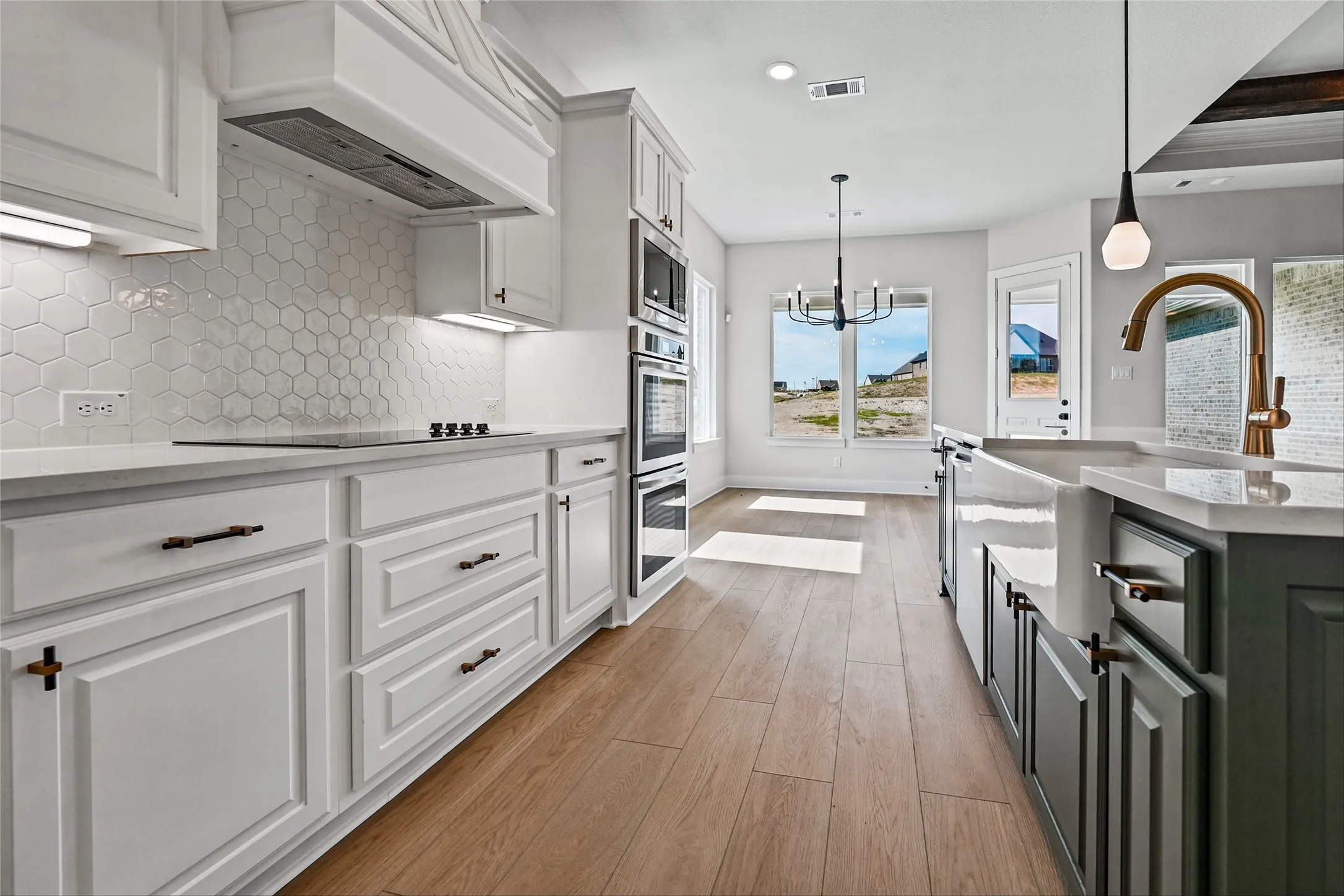 Kitchen featuring light wood-finish flooring, white cabinetry, hexagon tile backsplash, and a farmhouse-style sink with a gold-tone faucet