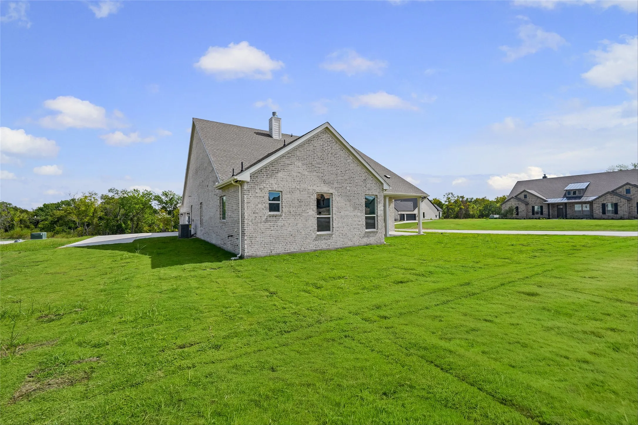 Expansive green lawn surrounding a light-colored brick exterior with a gray shingle roof