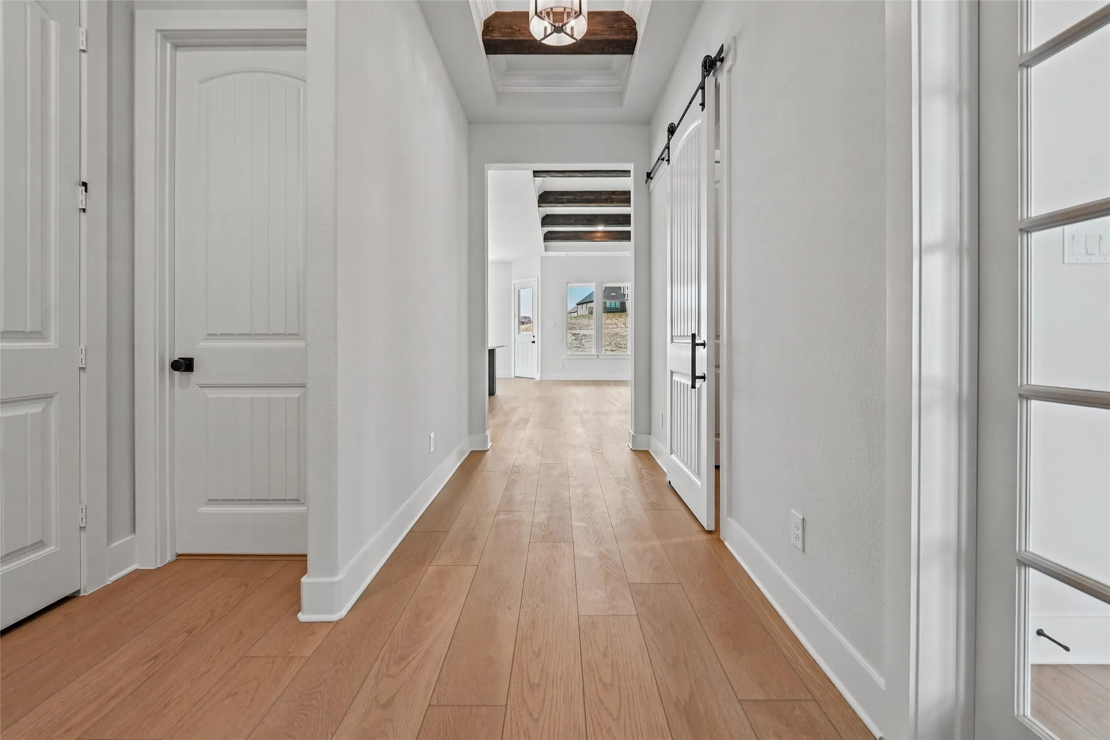 Hallway featuring wood-finish flooring, white walls, white trim, a barn door with black hardware, and a coffered ceiling with a wood-beamed detail
