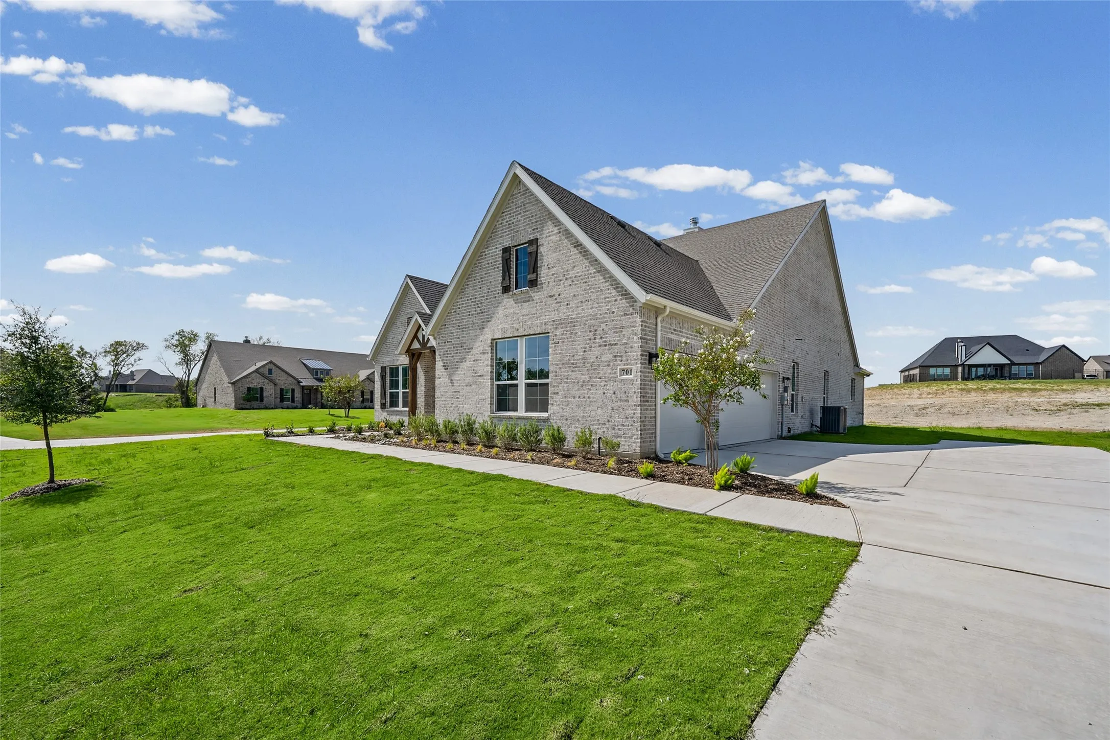 Light brick exterior with dark shingle roof, attached two-car garage, concrete driveway, and front landscaping