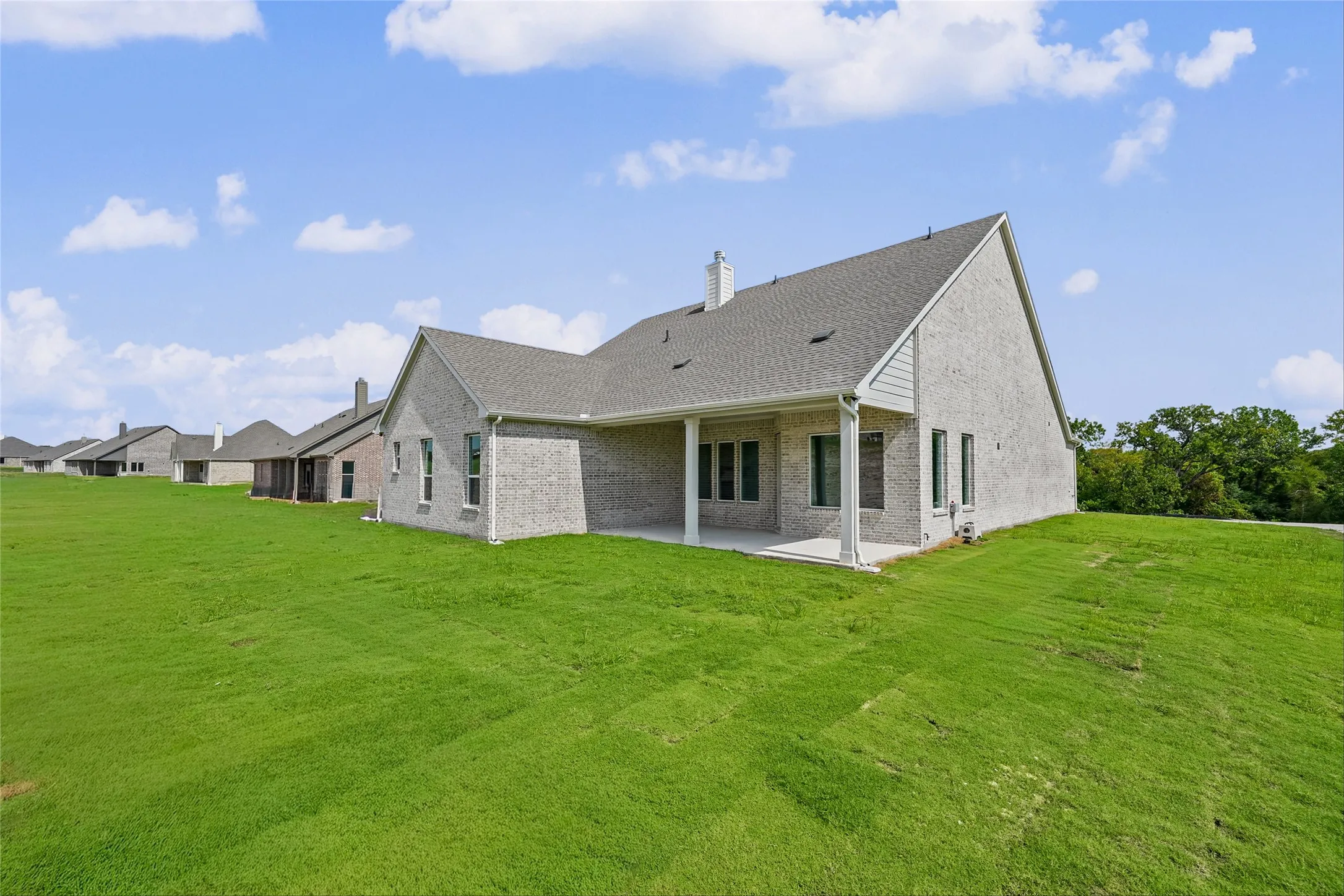 Brick exterior construction featuring a covered patio, multiple windows, and a large green lawn