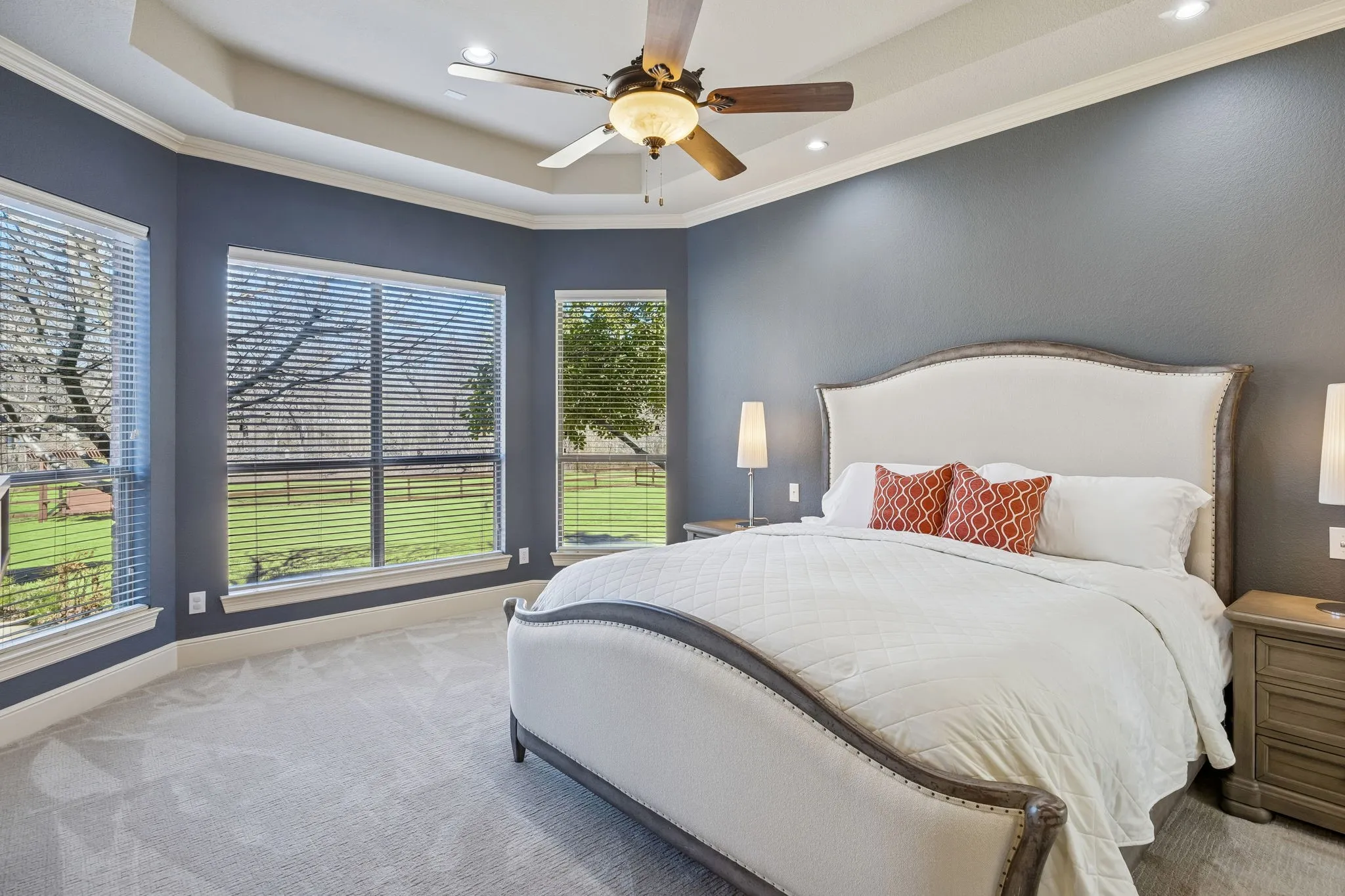 This spacious and serene primary bedroom features a tray ceiling and large windows that overlook the flourishing backyard.