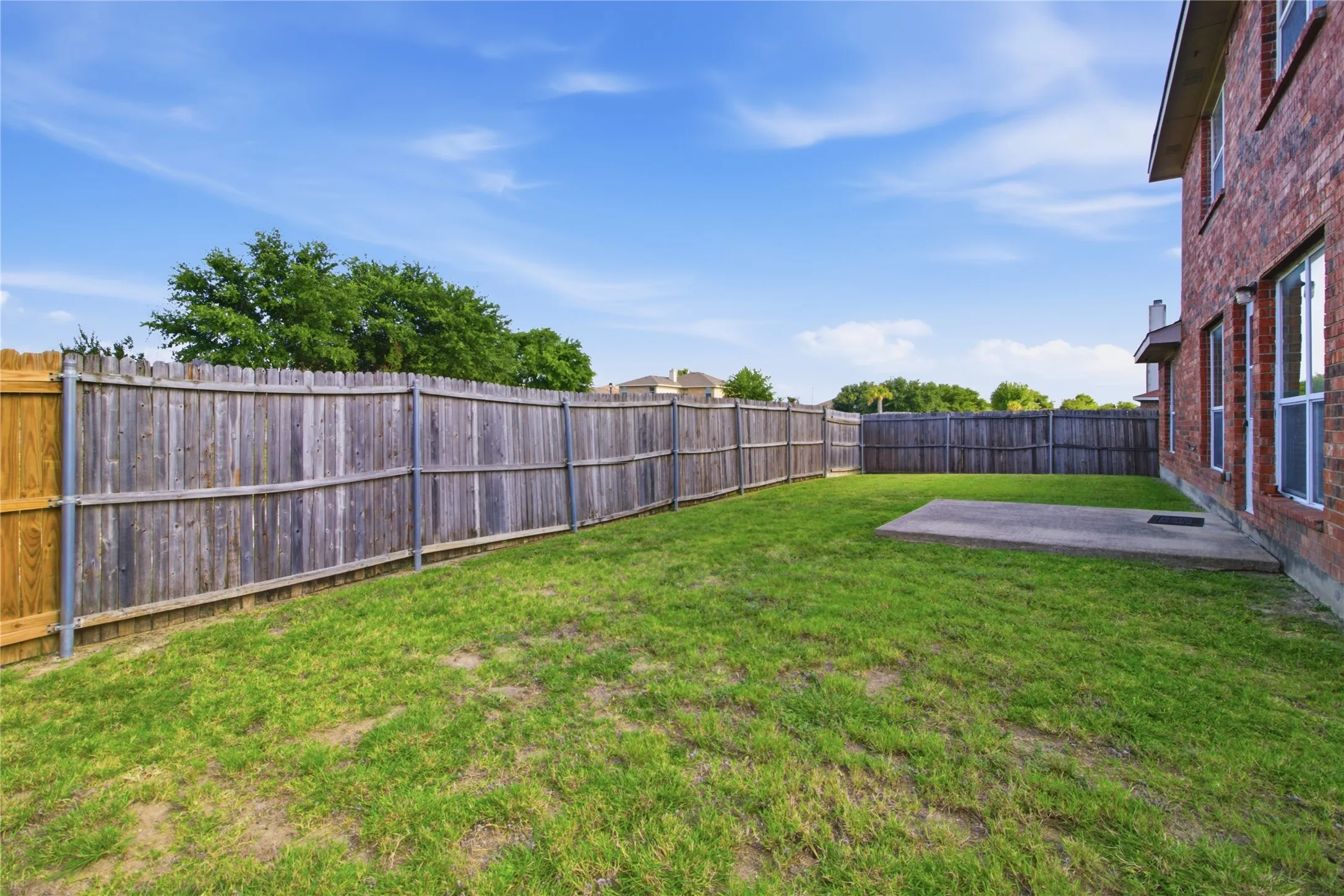 Spacious backyard with a grass lawn, privacy fencing, and a concrete patio