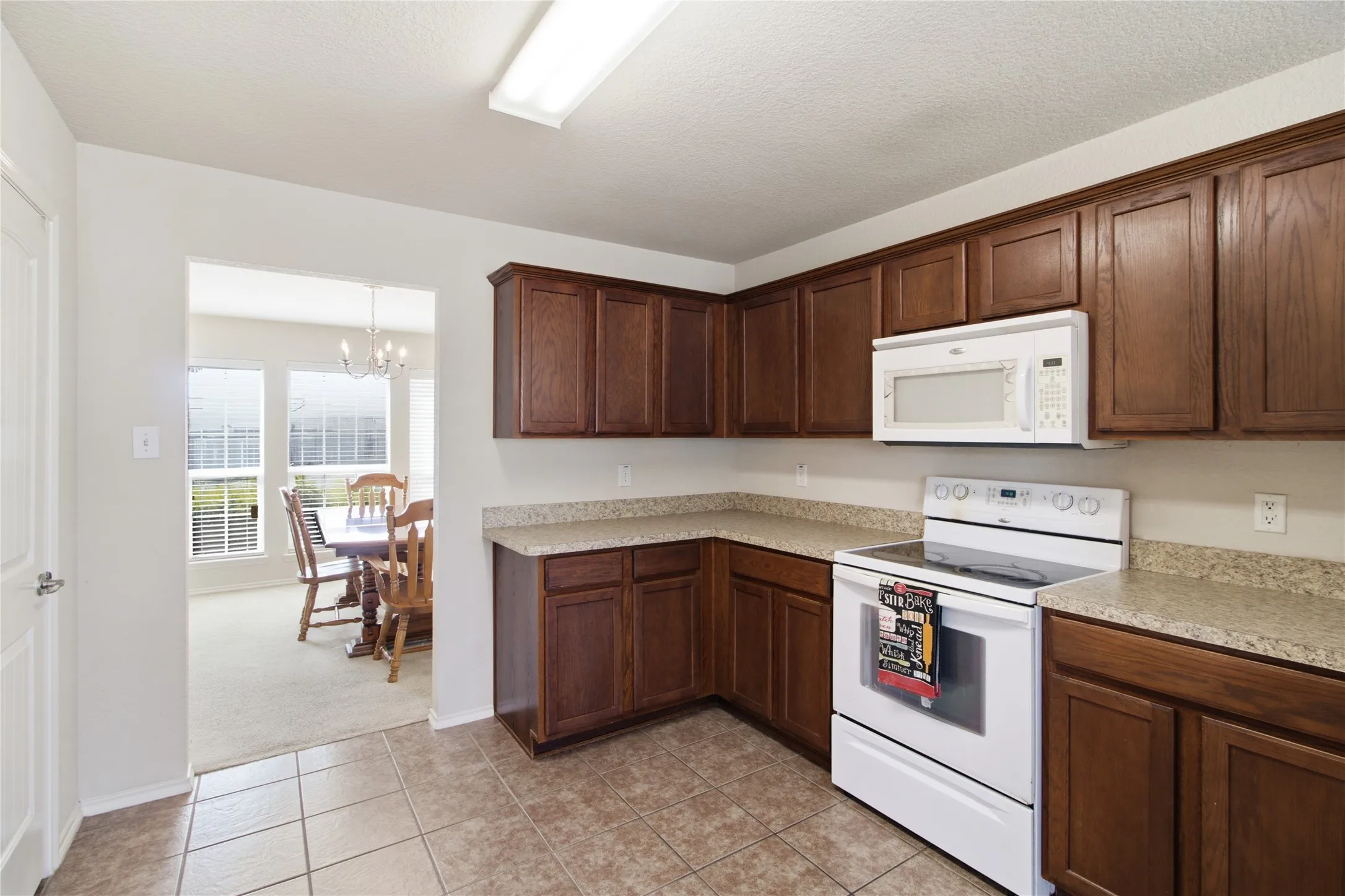 Kitchen featuring ample wood-finish cabinetry, light-toned countertops, and a white oven/range with an above-range microwave