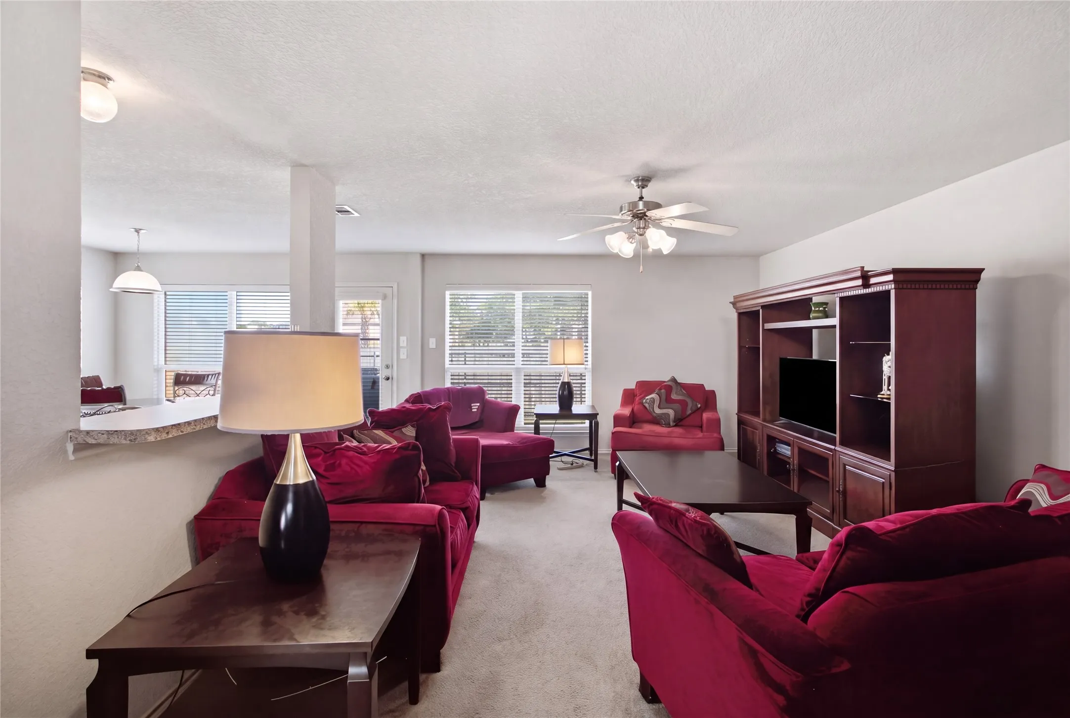 Spacious living area featuring carpet flooring, a ceiling fan with integrated lighting, and multiple windows for natural light