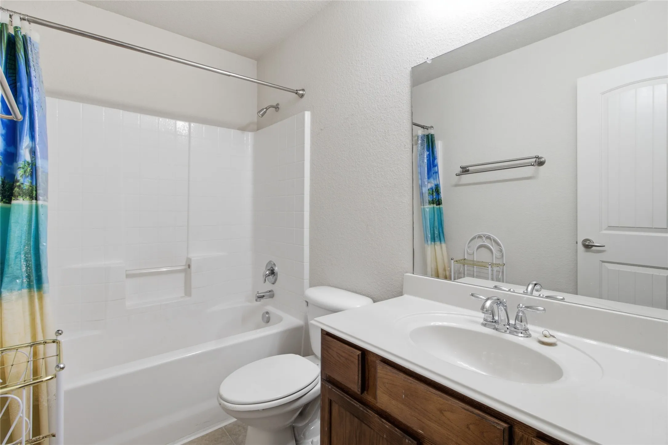 Bathroom featuring a white bathtub with a shower, a toilet, a vanity with a white countertop and an integrated sink, and a large mirror