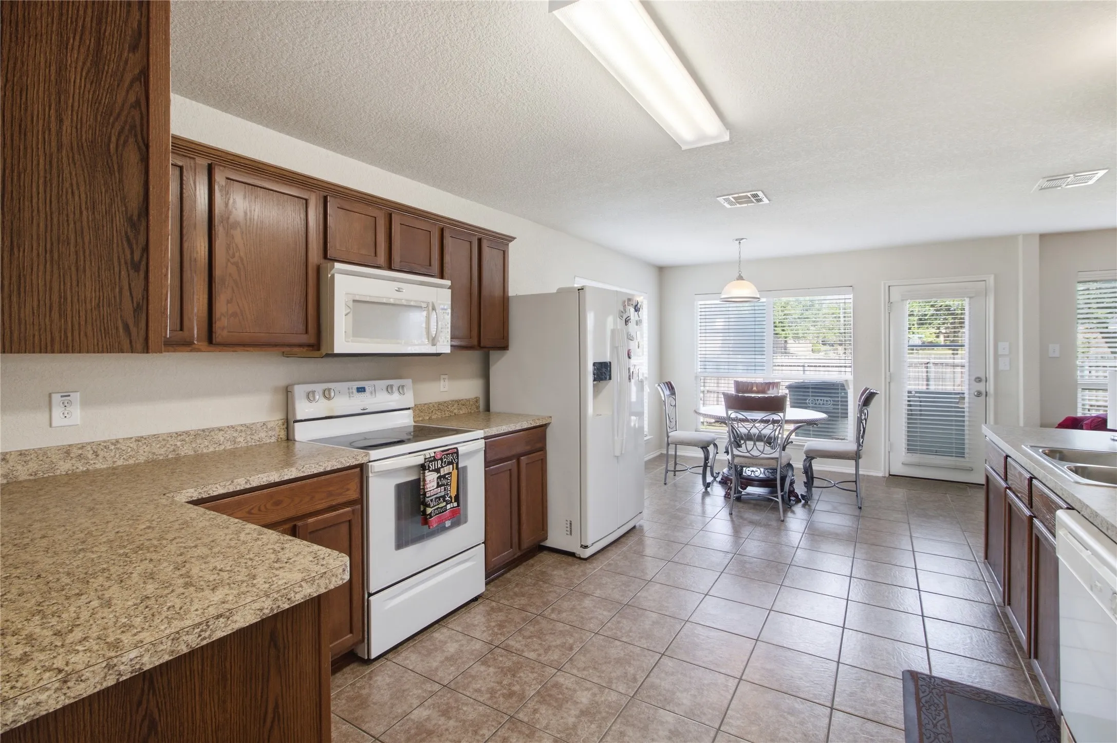 Spacious kitchen featuring wood cabinetry, stone-look countertops, and tile flooring