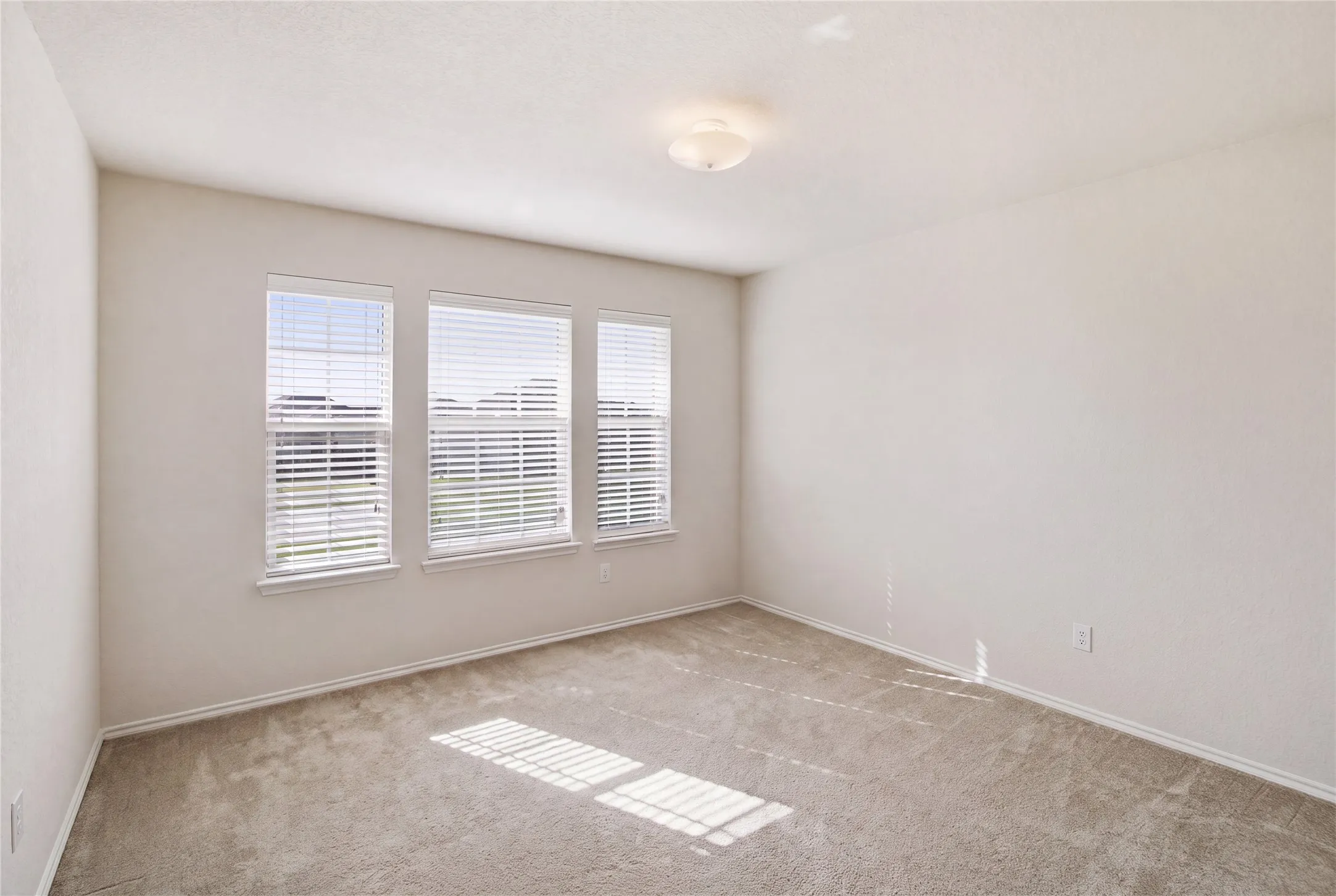 Bright room featuring three individual windows with white blinds, neutral wall paint, and light-colored carpet