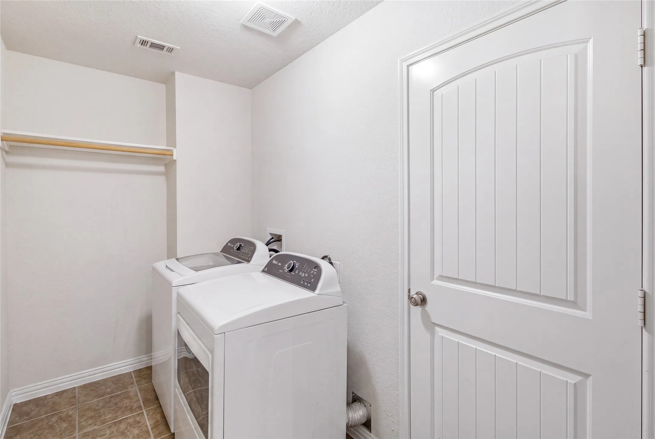 Dedicated utility space featuring a white paneled door, neutral tile flooring, and a built-in hanging rod