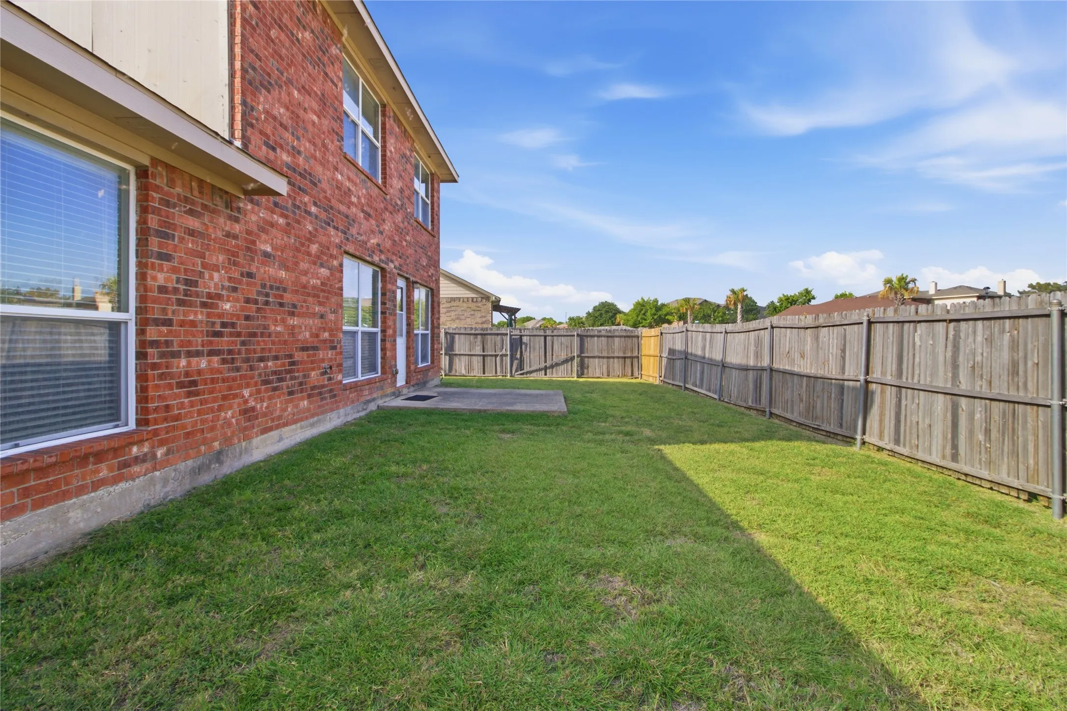 Expansive backyard featuring a manicured lawn, brick exterior, and a concrete patio