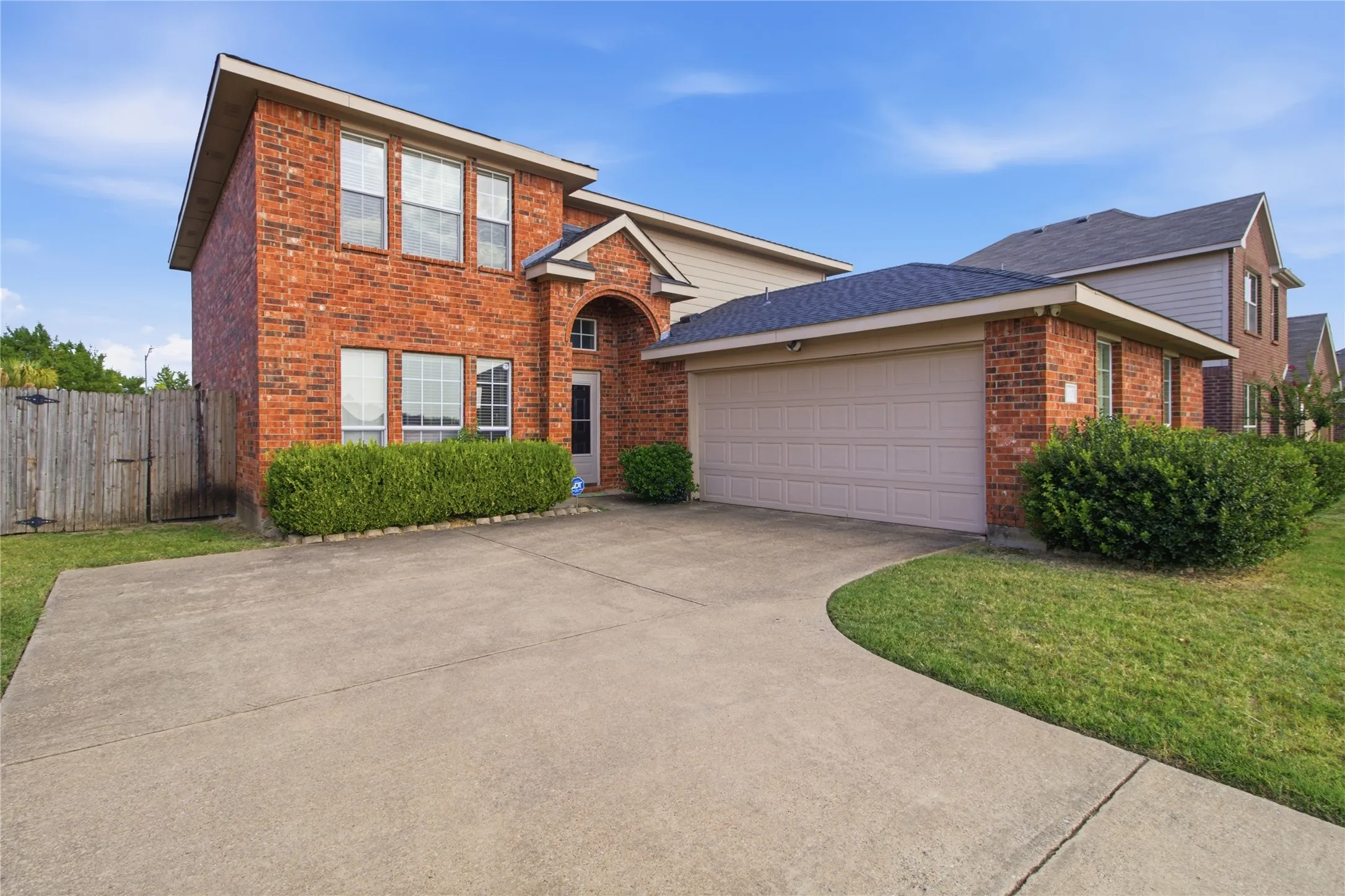 Brick exterior featuring a two-car garage, concrete driveway, and established front landscaping