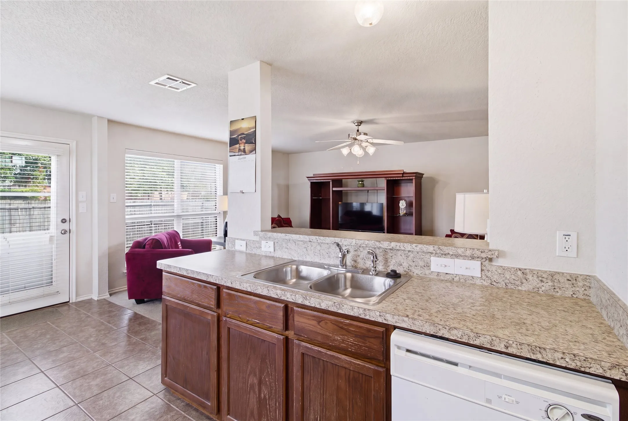 Kitchen featuring a double stainless steel sink, light-toned countertop, and wood-finish cabinetry