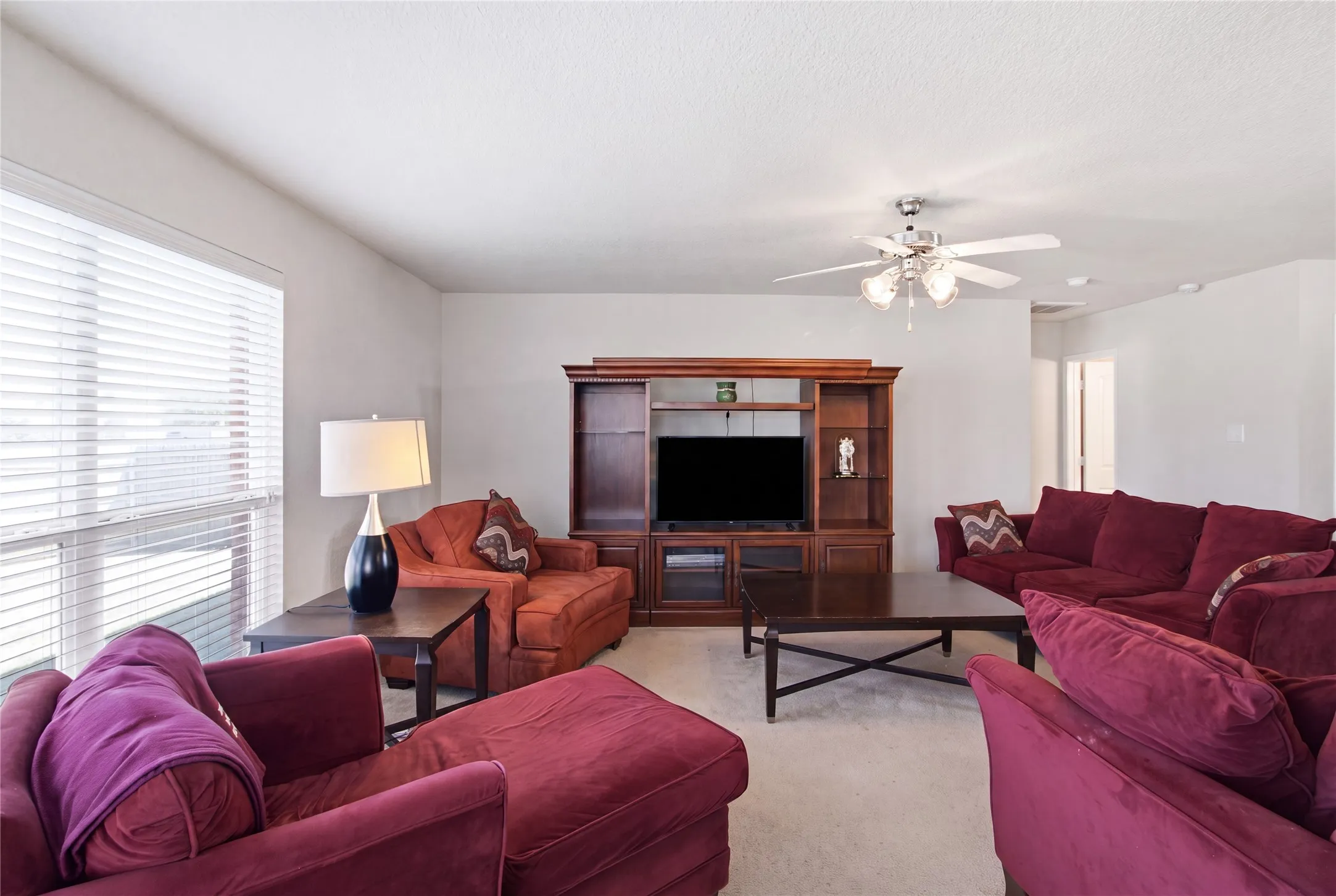 Living room featuring a built-in entertainment center with shelving and cabinet storage, ceiling fan, and carpeted flooring
