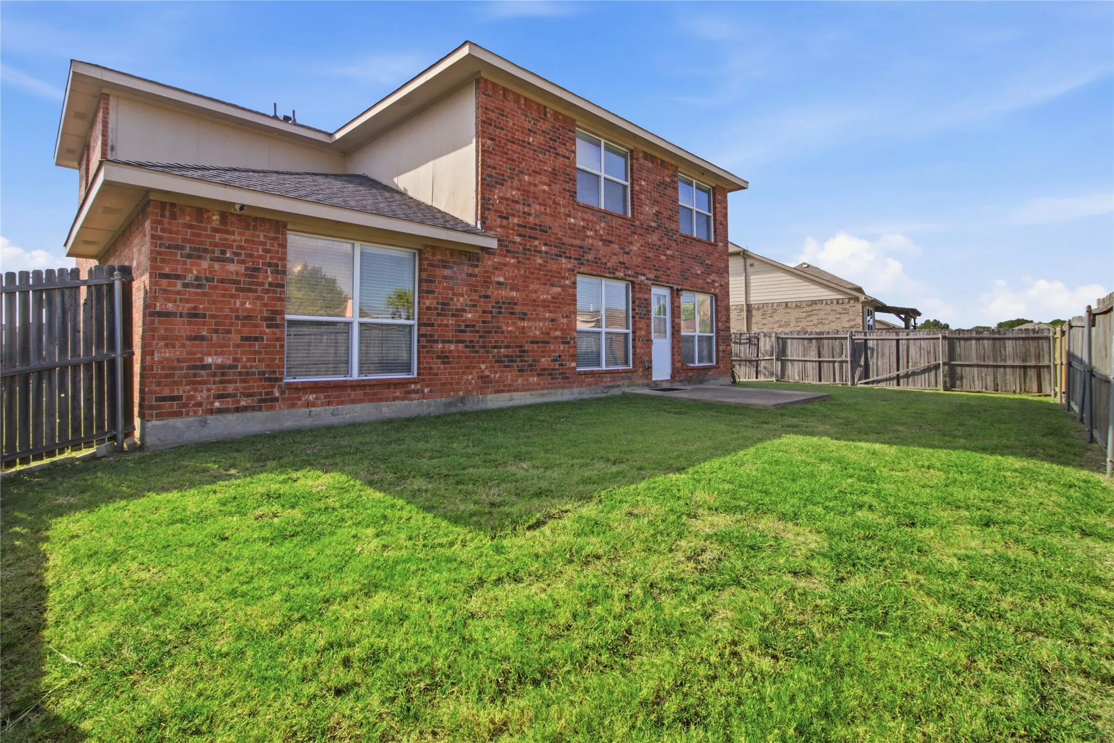 Spacious fenced backyard featuring a concrete patio and brick exterior