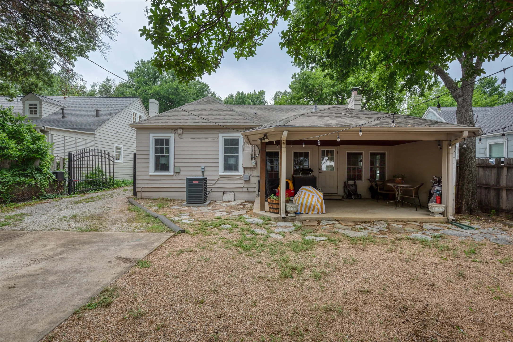Exterior featuring a covered patio with string lighting, multiple windows with white trim, and a gravel driveway