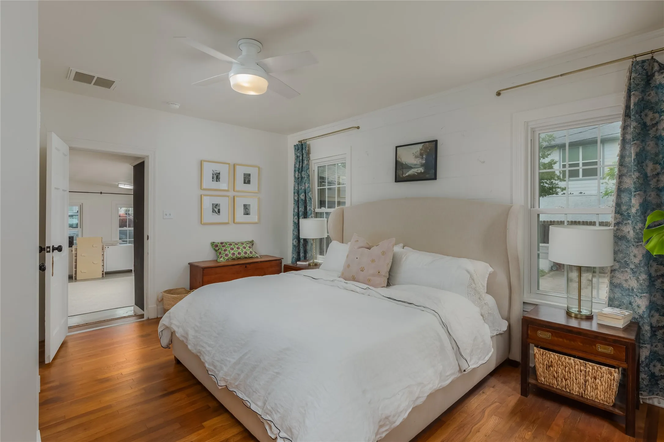 Bedroom featuring hardwood flooring, white walls, two windows, and a ceiling fan with integrated lighting