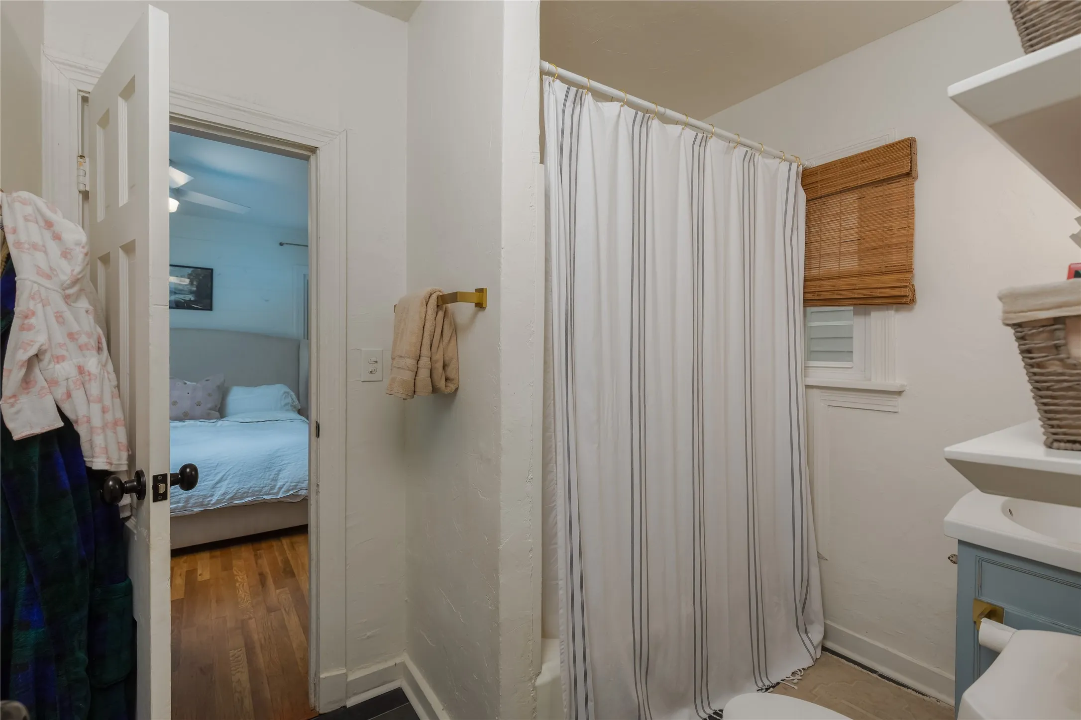 Bathroom with a shower/tub combination, a vanity with an undermount sink, and a window with a woven wood shade