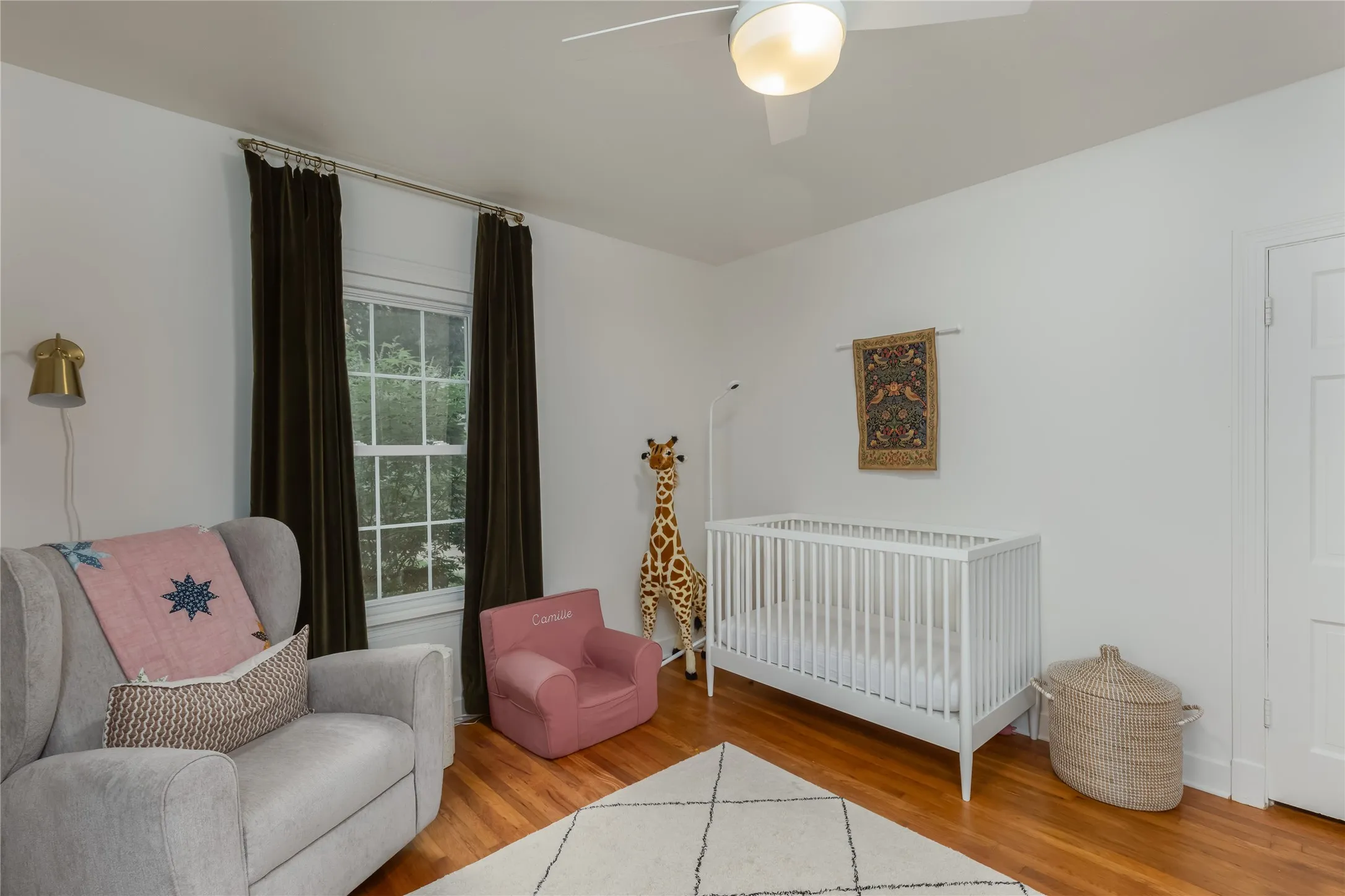 Hardwood flooring extending throughout, a ceiling fan with integrated lighting, and a window with white trim and dark curtains
