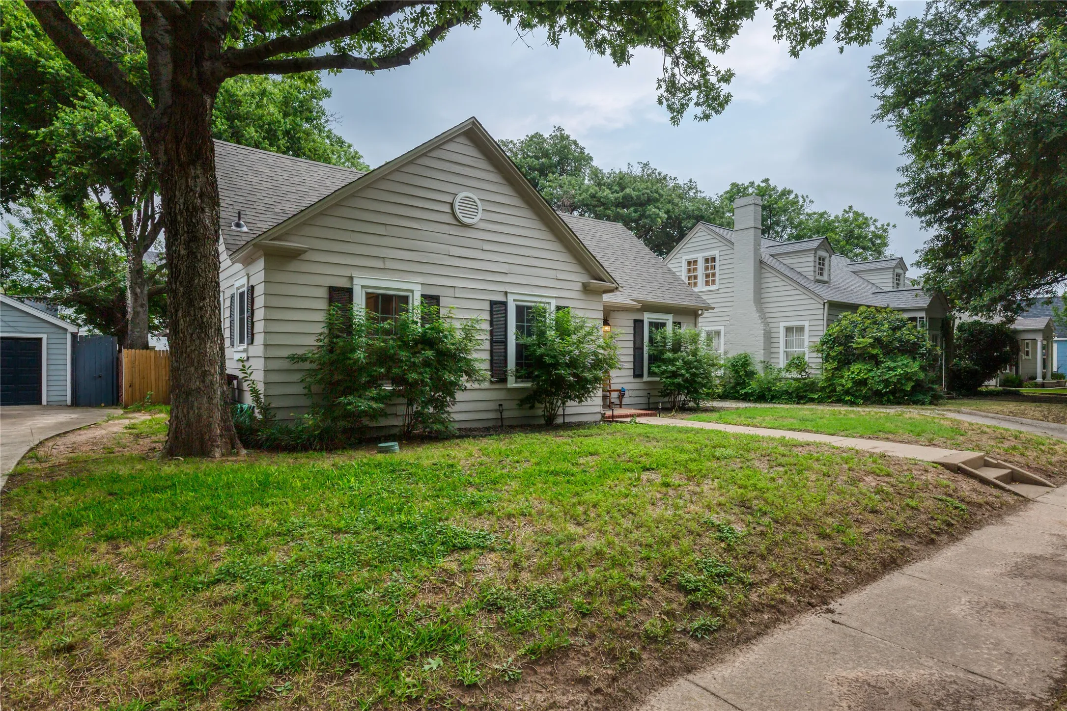 Single-story residence featuring light-toned siding, dark shutters, and a gabled roofline