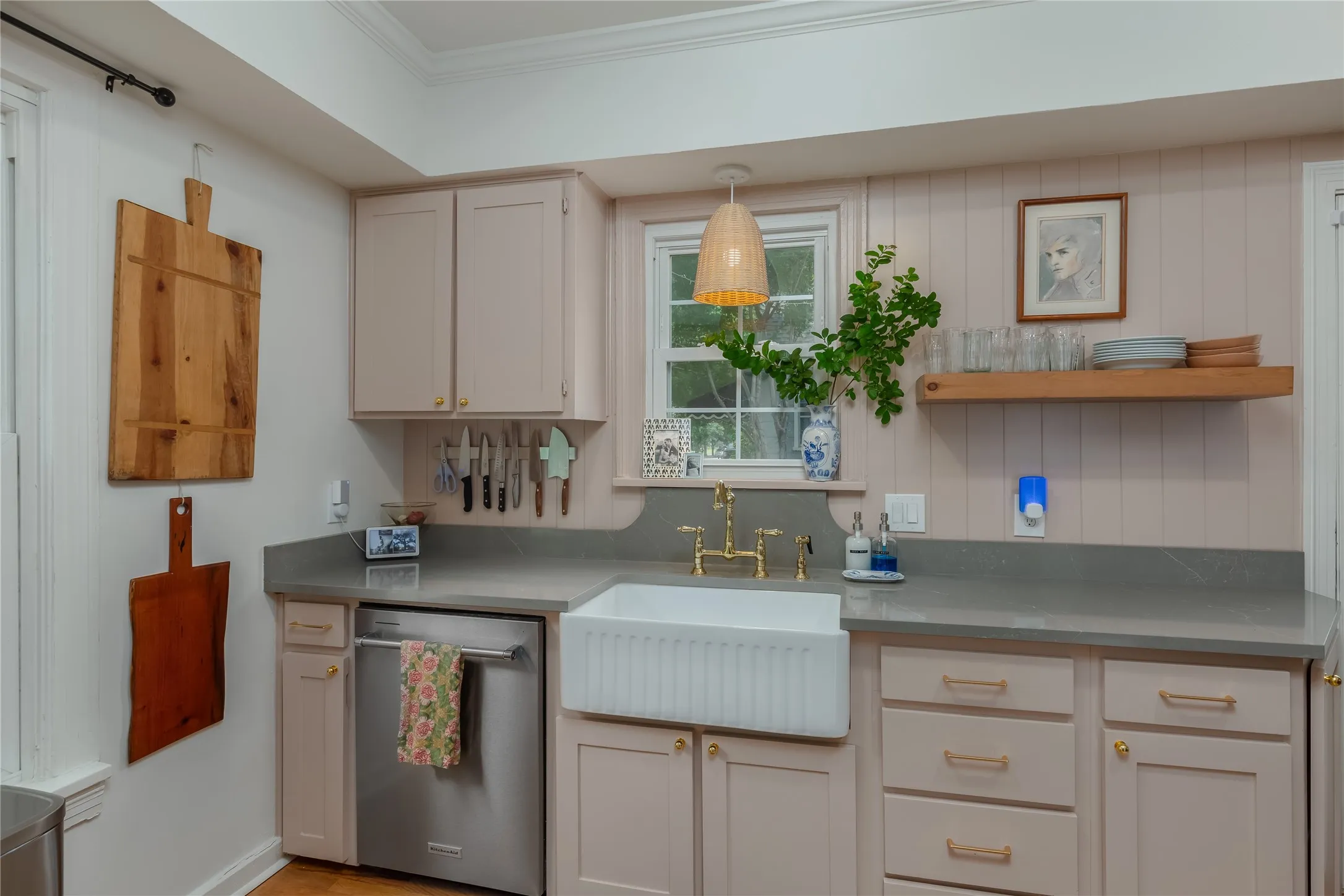 Kitchen featuring a farmhouse sink with brass fixtures, light gray countertops, and light pink cabinetry with gold hardware