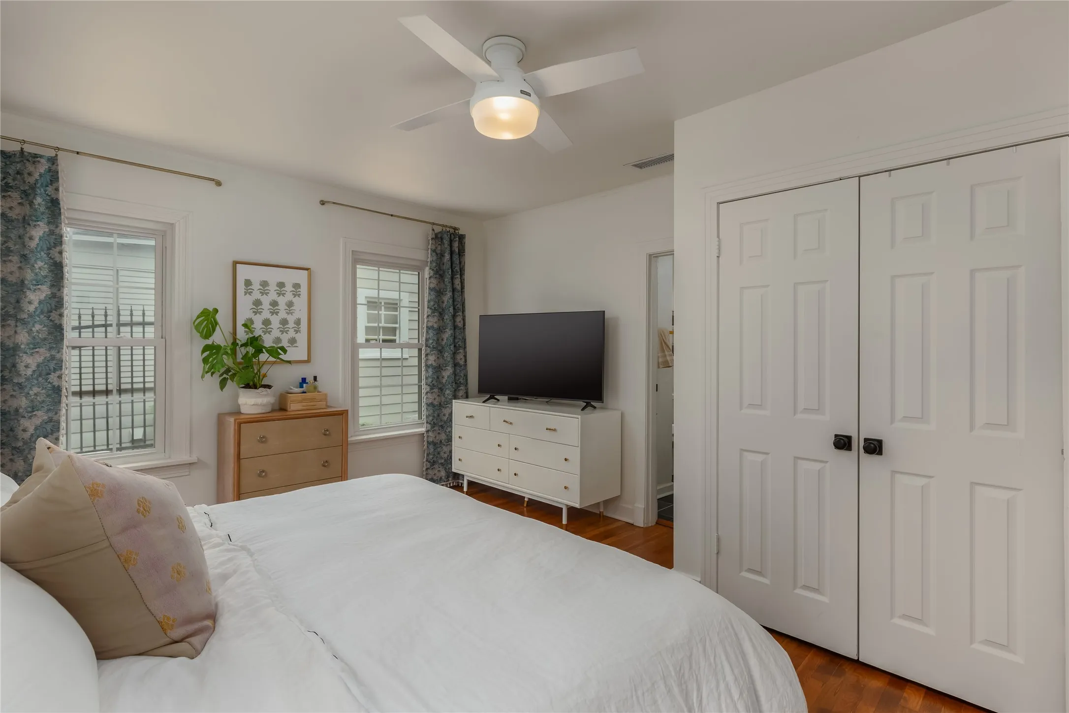 Bedroom featuring two paneled windows, a modern ceiling fan with integrated lighting, wood-finish flooring, and a six-panel bi-fold closet door