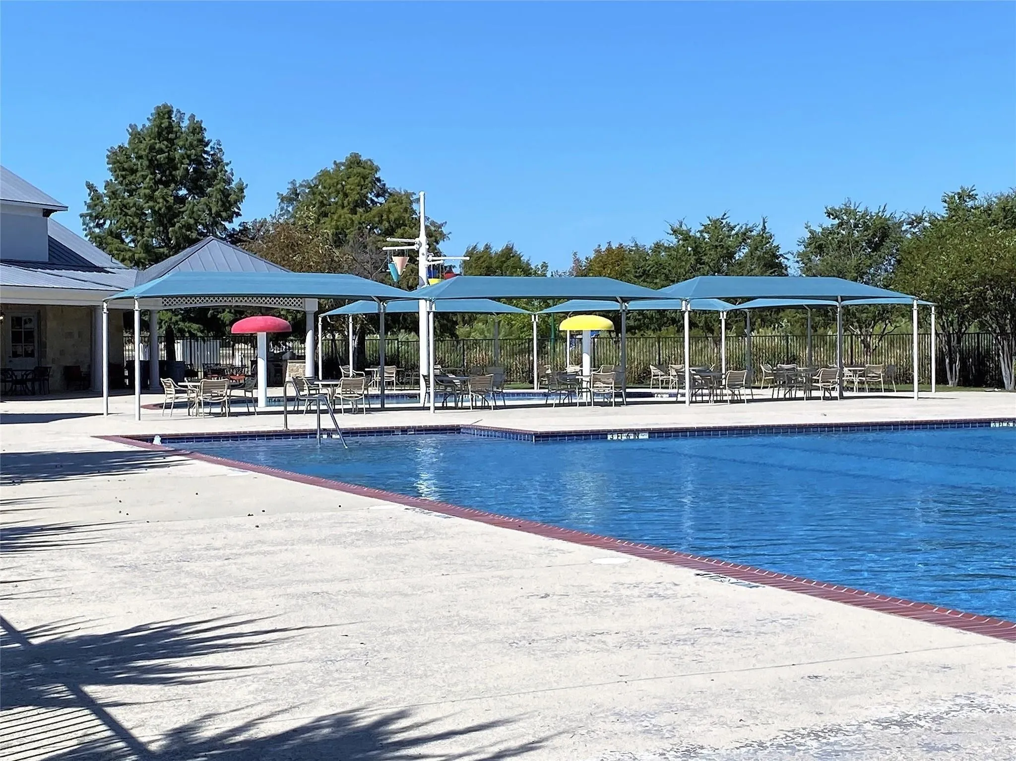 Outdoor swimming pool with integrated shade structures, multiple seating areas, and a concrete deck