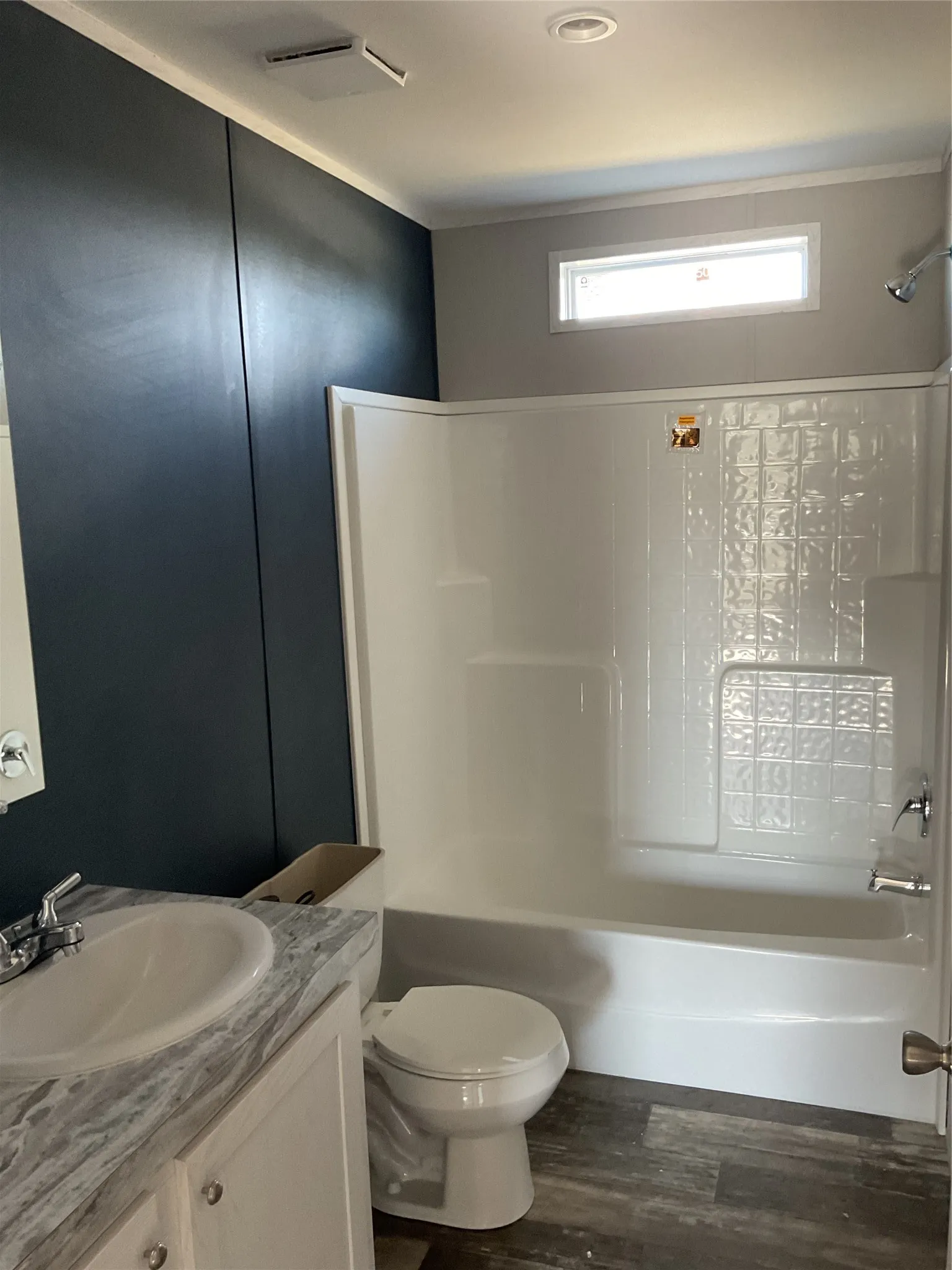 Bathroom featuring a white vanity with an integrated sink, a full shower-tub combination with textured glass block design, and wood-finish flooring
