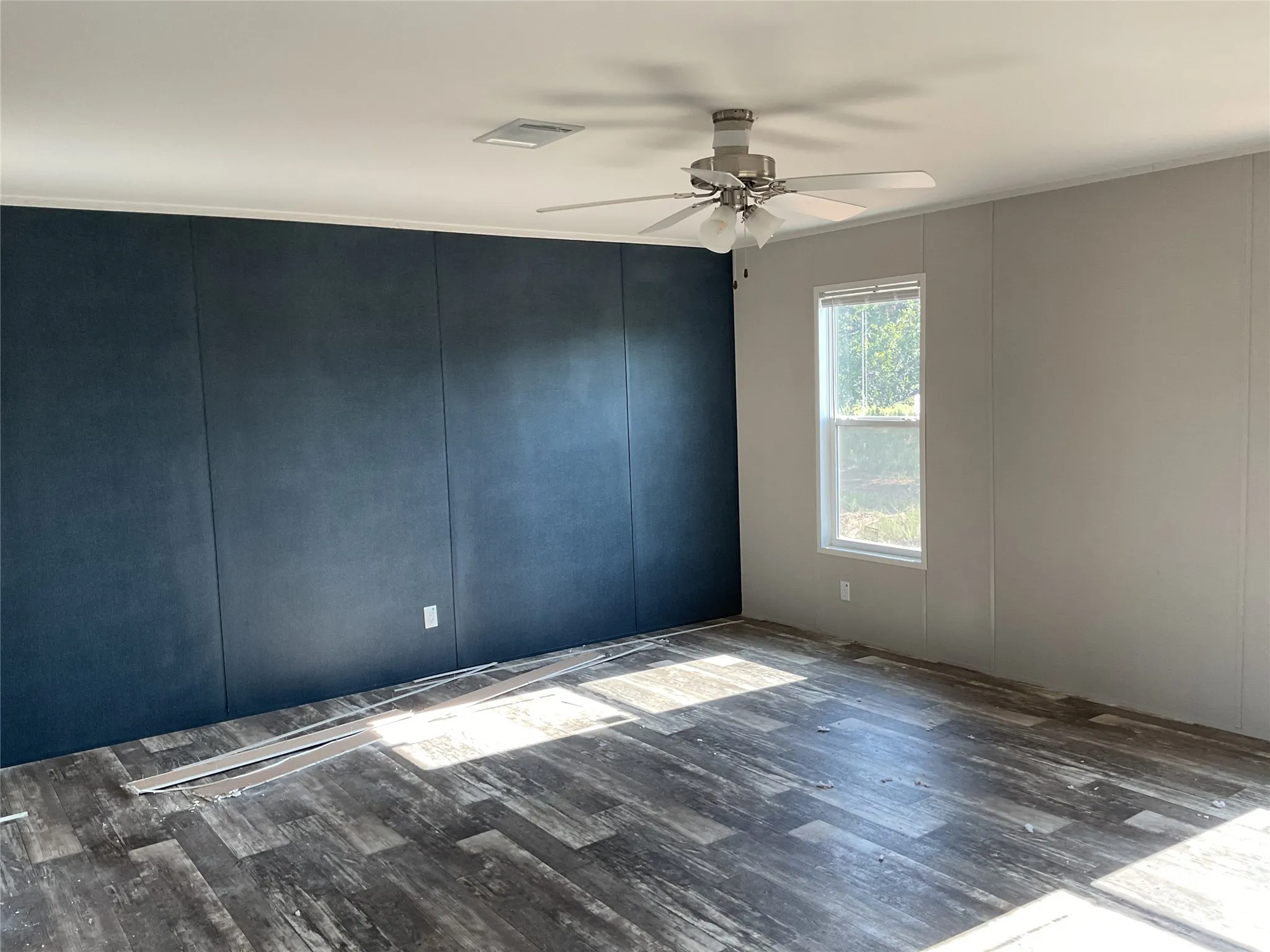 Interior space featuring wood-finish flooring, a contemporary ceiling fan with integrated lighting, and a prominent dark accent wall