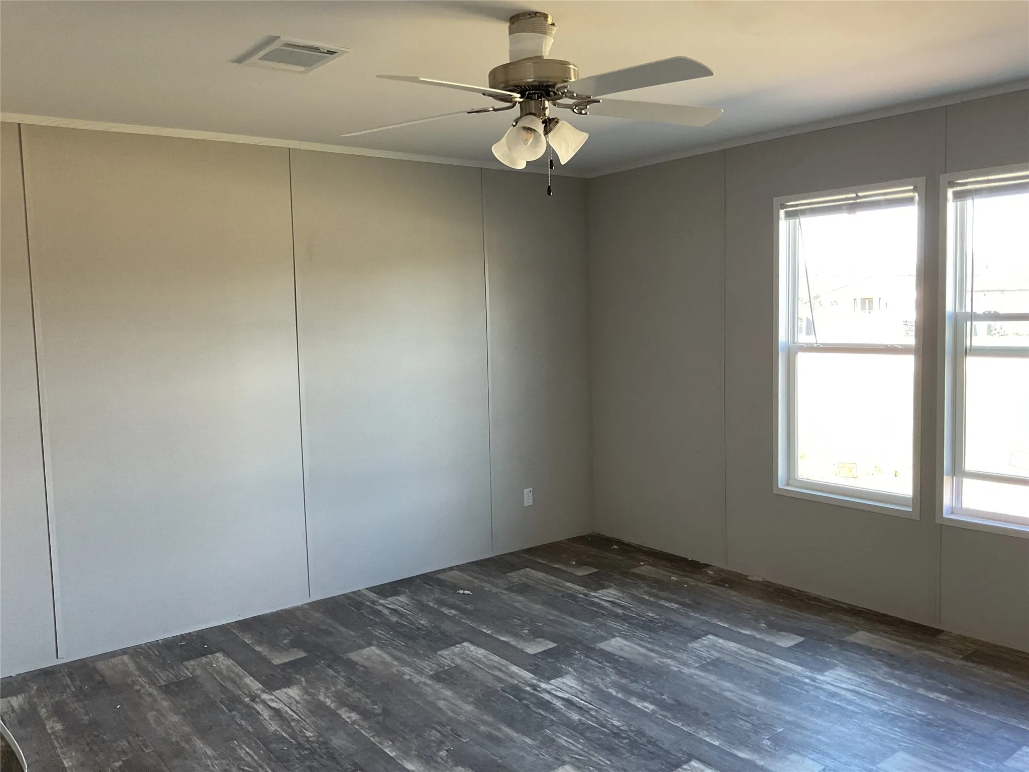 Room with wood-finish flooring, two large windows, a ceiling fan with integrated lighting, and crown molding