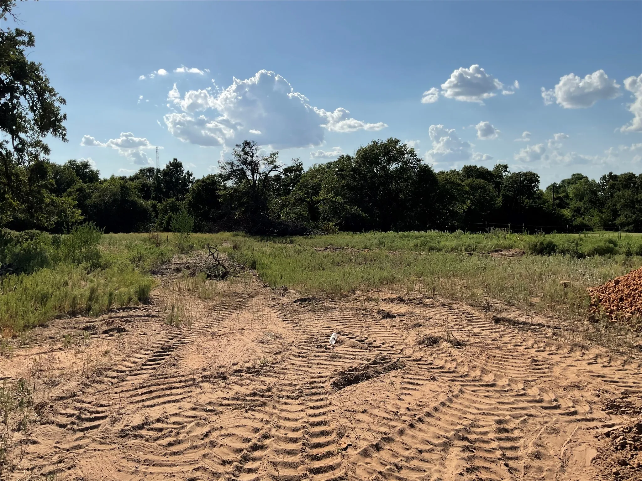 Expansive land parcel featuring cleared ground with visible tire tracks, surrounded by mature trees and natural vegetation