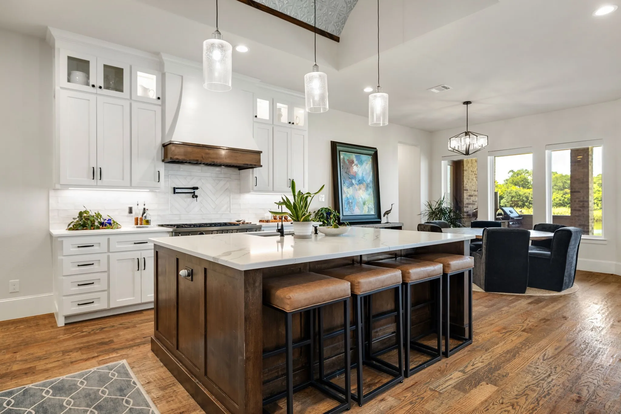 Spacious kitchen featuring a large central island with a quartz countertop, white shaker-style cabinetry, a built-in range with a wood and white vent hood, and wood-finish flooring throughout