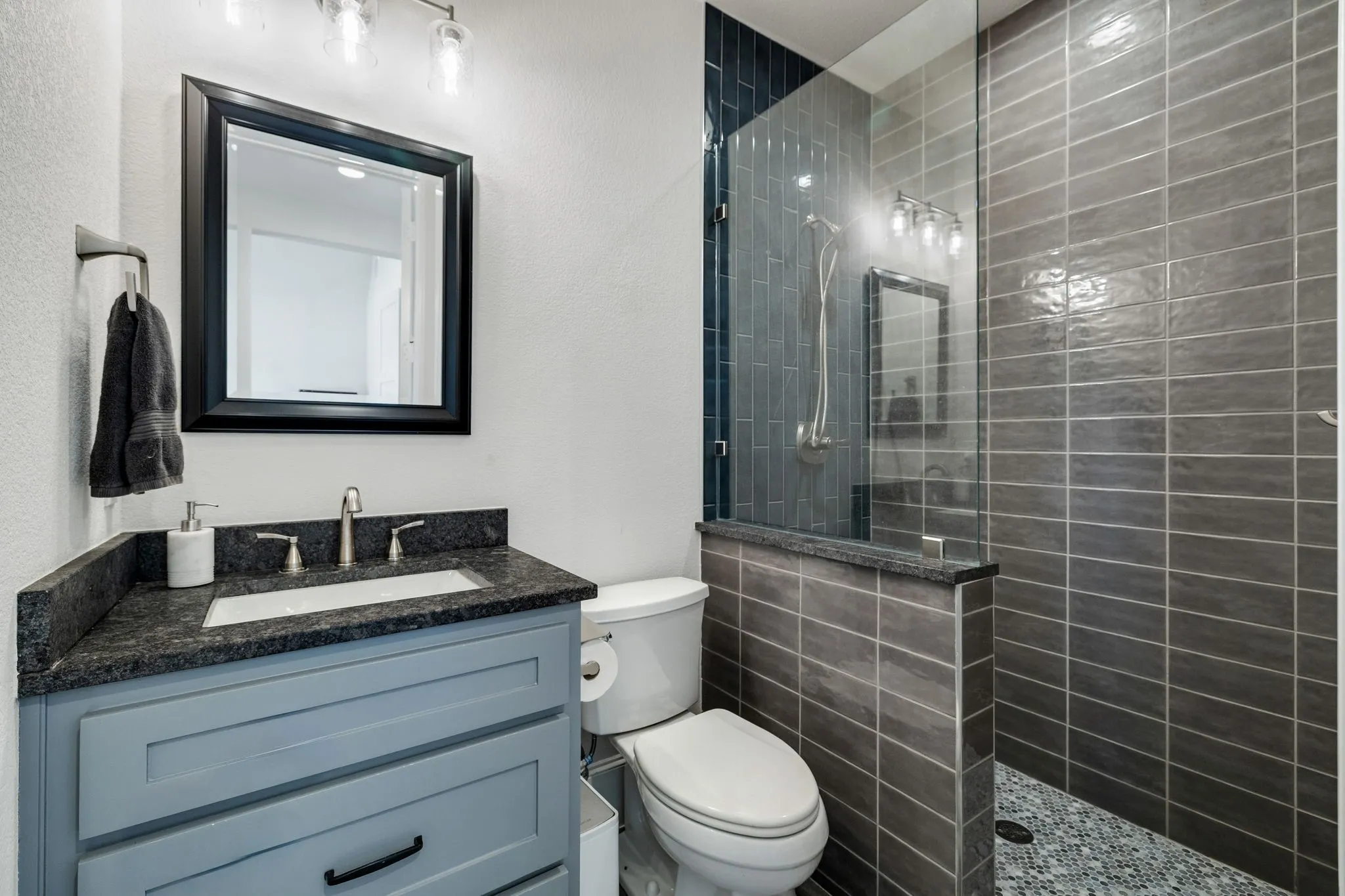 Modern bathroom featuring a glass-enclosed shower with gray subway tile walls and a pebble-finish floor
