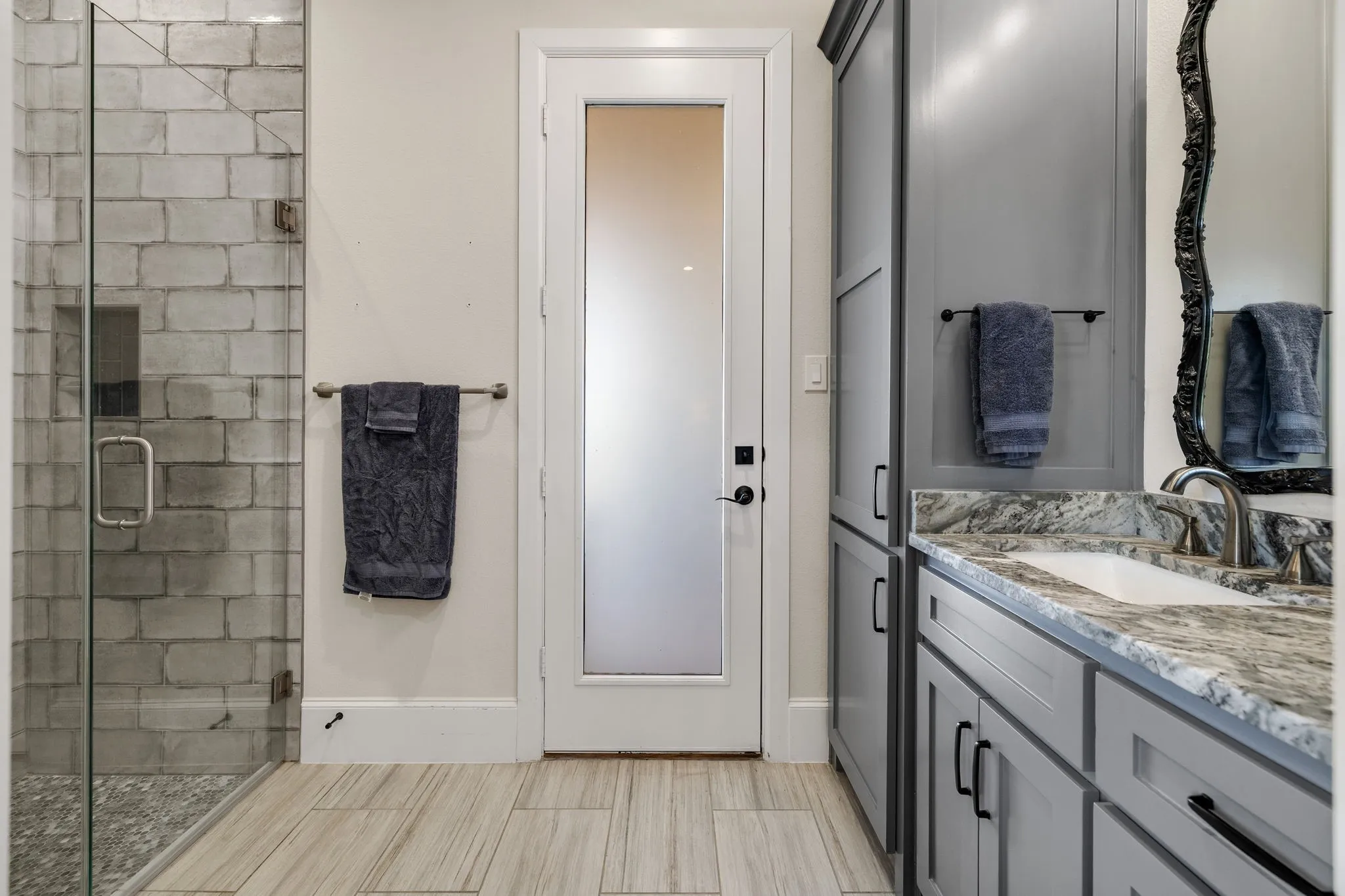 Bathroom with a glass-enclosed shower, featuring a light-toned brick-style tile surround and a pebble-style floor and access to the back patio