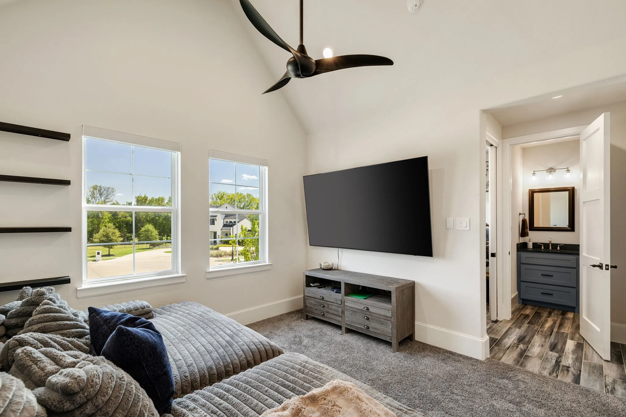 Vaulted ceiling room with two double-hung windows, wall-mounted shelving, and a contemporary ceiling fan