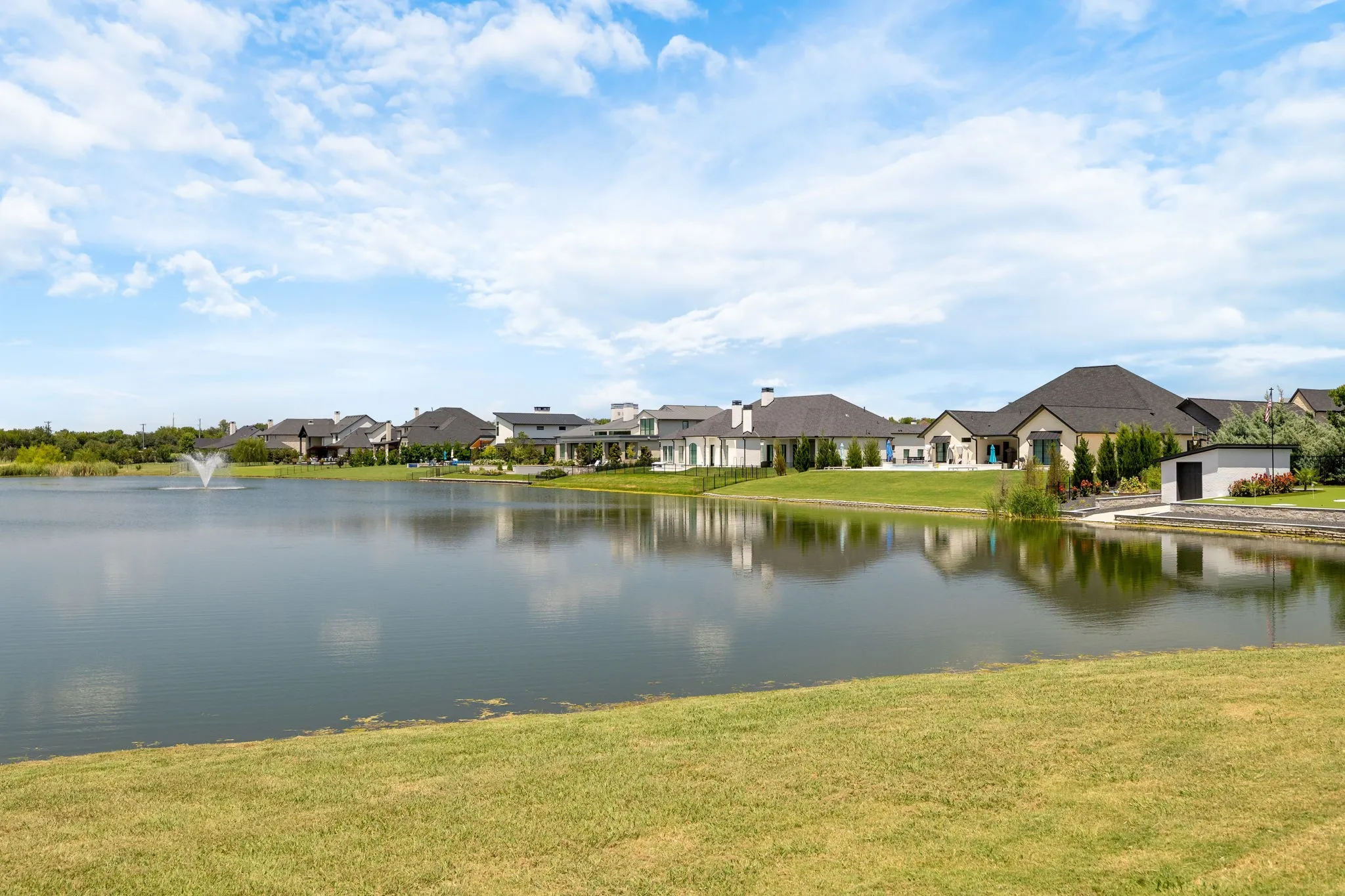 Manicured green lawn bordering a calm body of water with a fountain