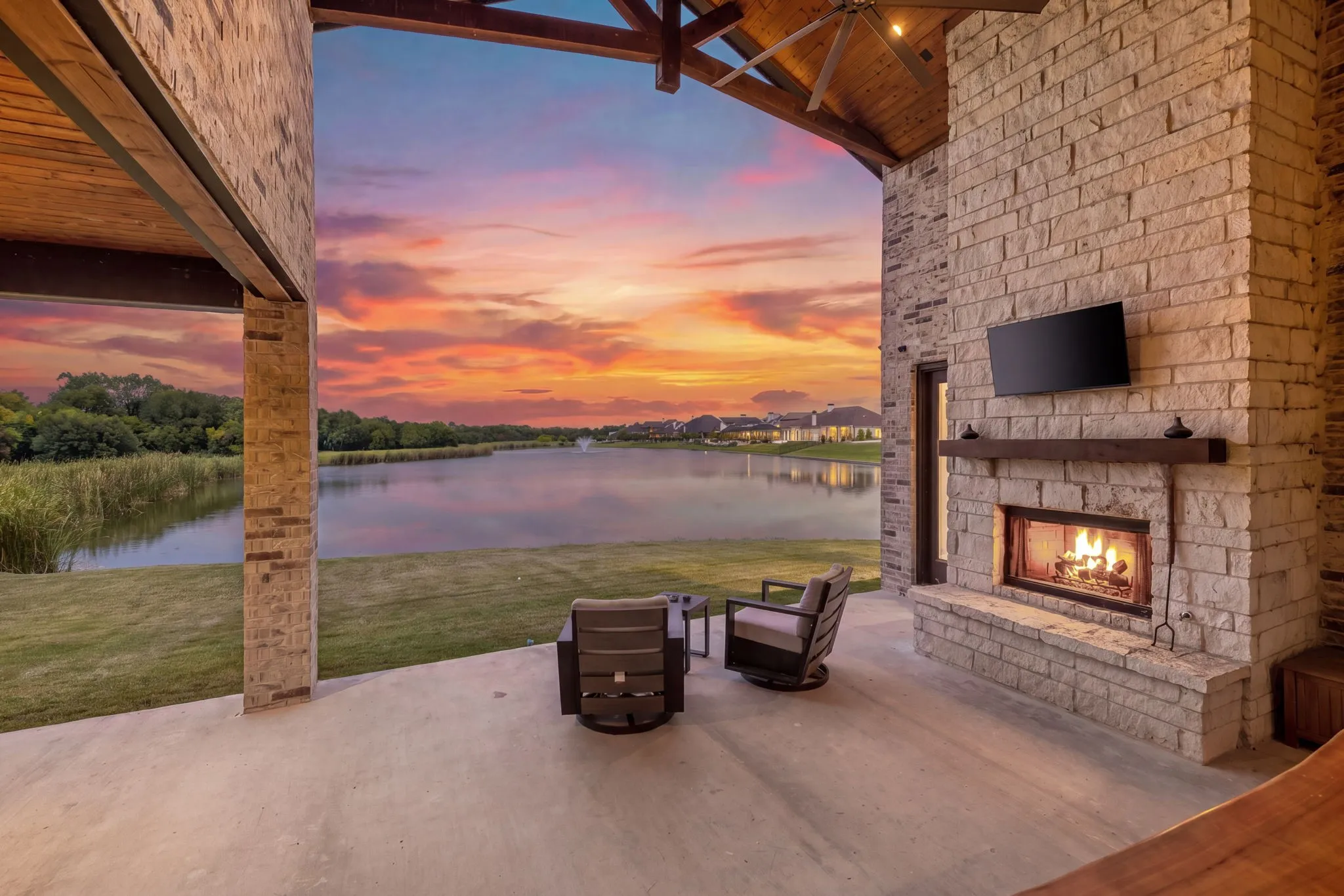 Covered outdoor patio featuring a stone-clad fireplace with a built-in television mount, a wood-finish vaulted ceiling with exposed beams, and a ceiling fan
Virtual Twilight