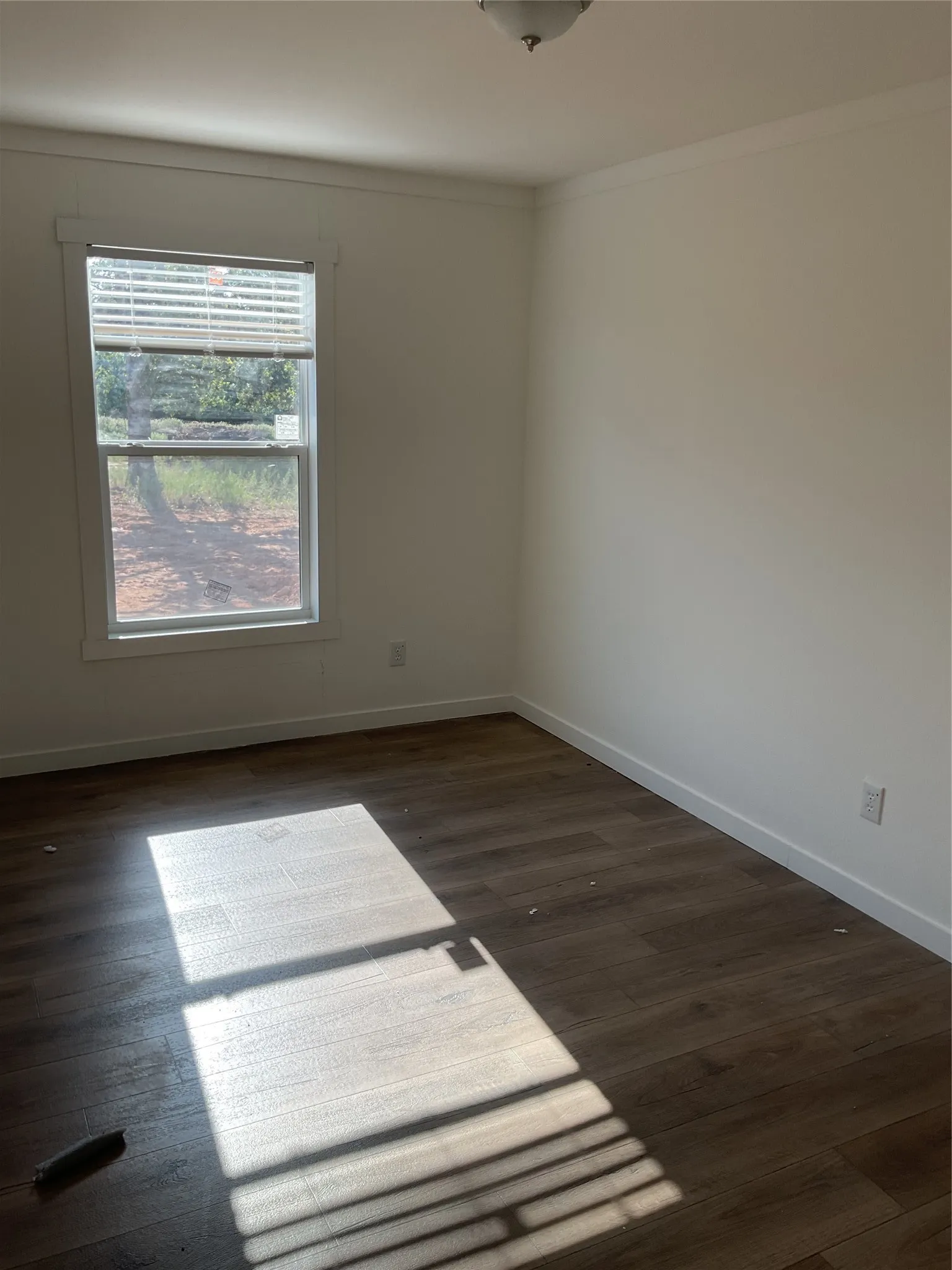 Room featuring wood-finish flooring, white walls, white baseboards, a single window, and a flush-mount ceiling light fixture