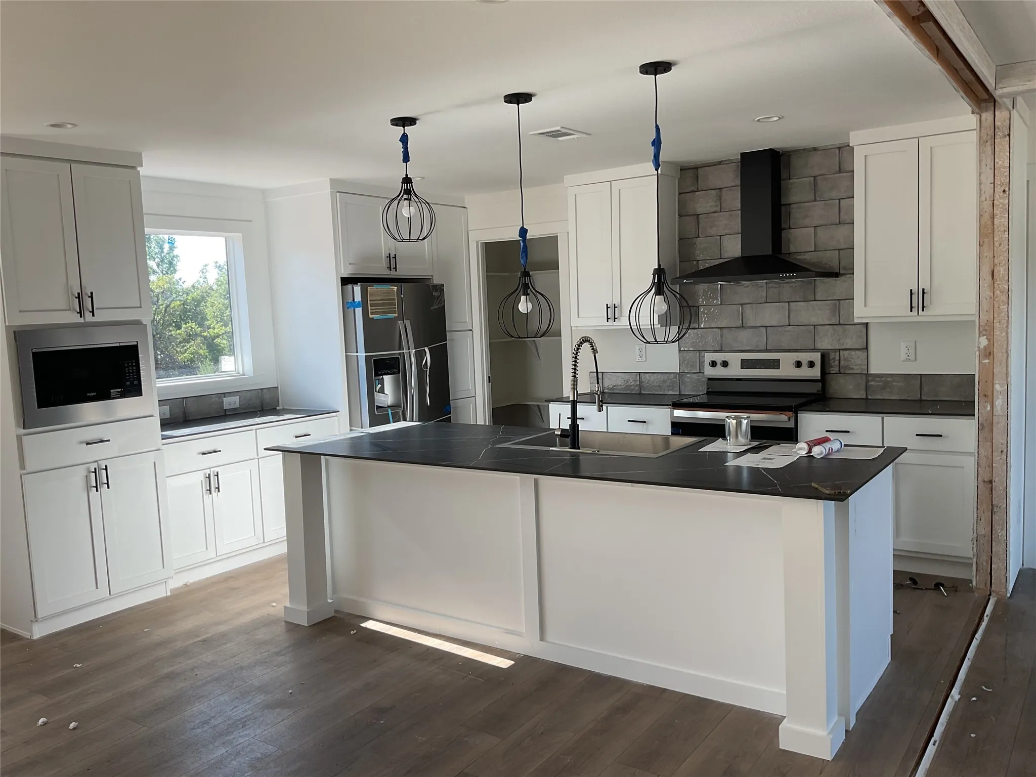 Kitchen featuring a large island with an integrated sink, white cabinetry, dark countertops, stainless steel appliances, and wood-finish flooring