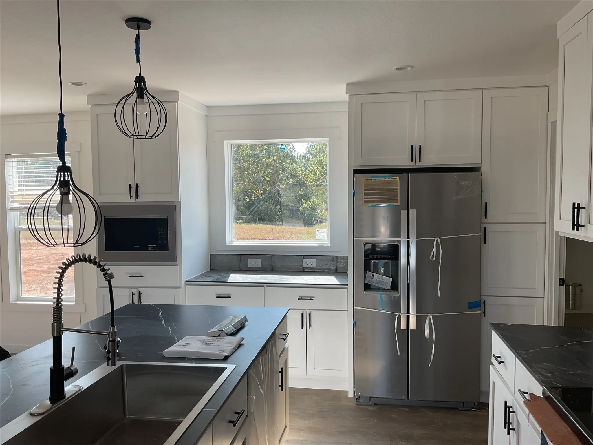 White cabinetry with matte black hardware, stainless steel appliances, dark countertops, and a kitchen island with an undermount sink