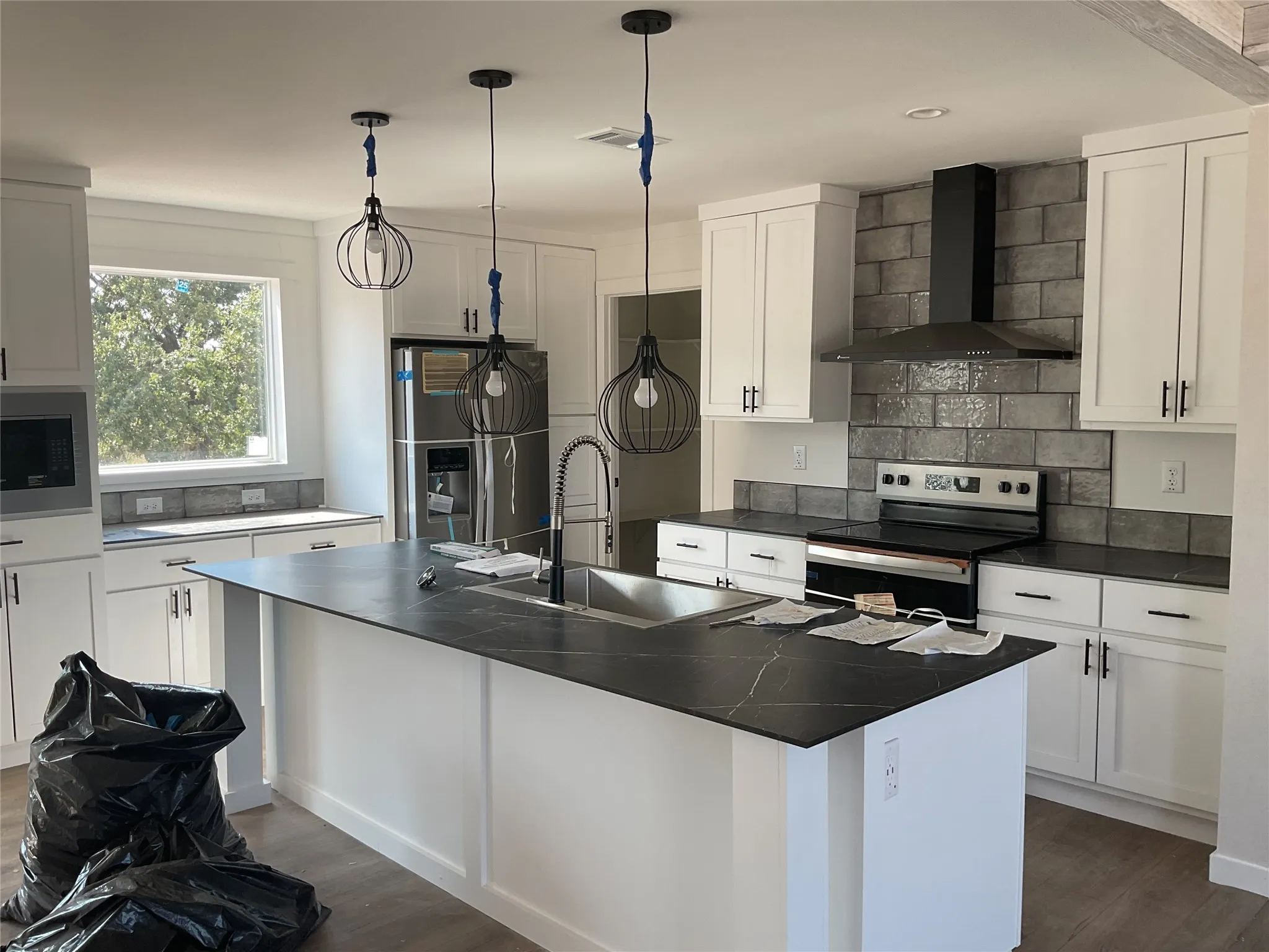 Kitchen featuring a central island with sink, white shaker cabinetry, dark countertops, and a subway tile backsplash