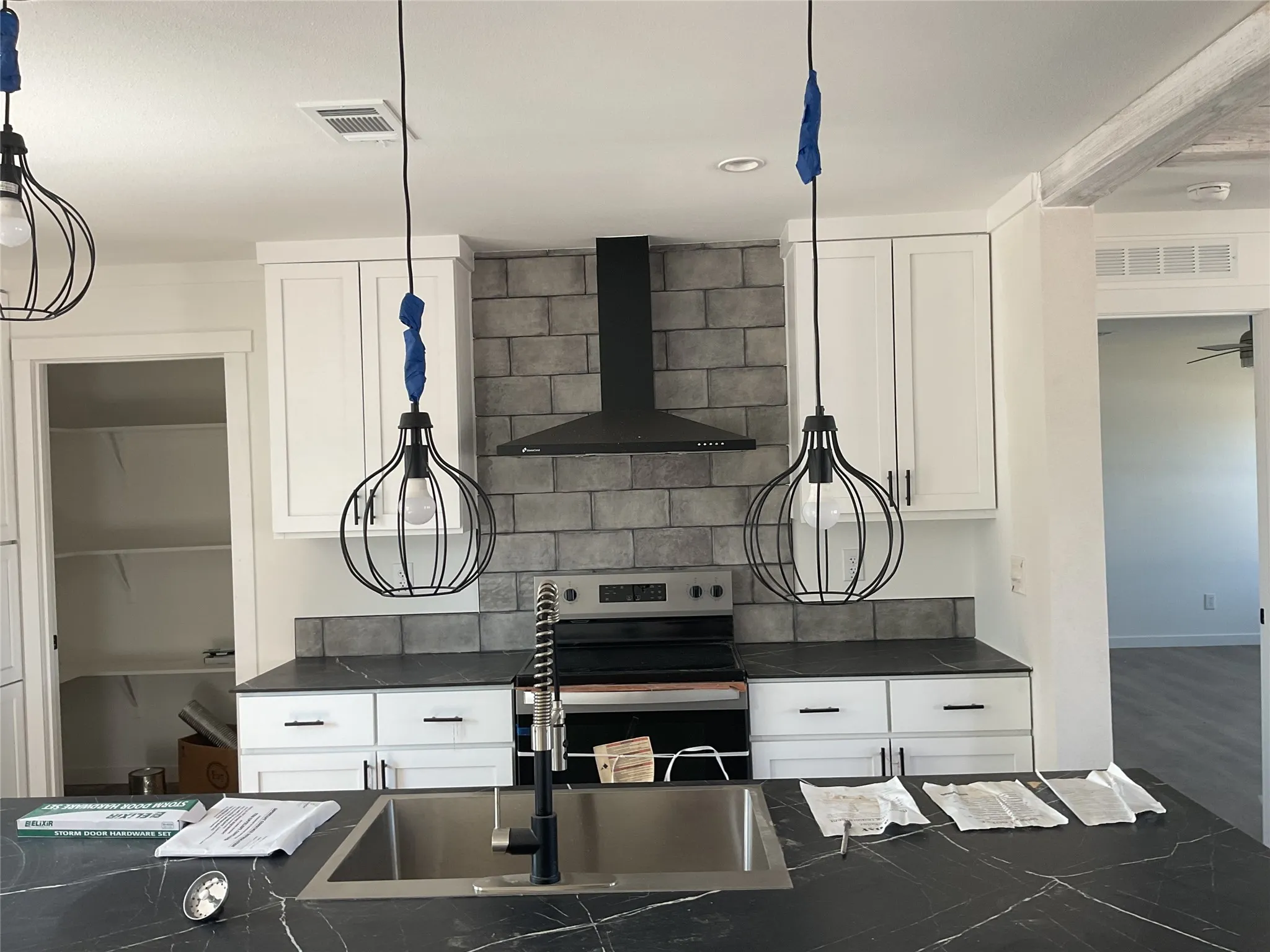 Kitchen featuring black marble-look countertops, white cabinetry, a stainless steel sink with a black pull-down faucet, and a black range hood with a gray tiled backsplash