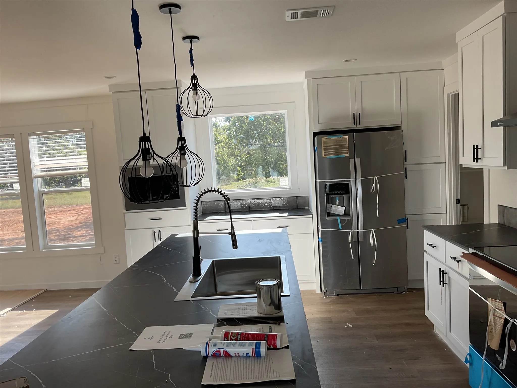 Kitchen featuring white cabinetry with dark hardware, dark countertops with light veining, stainless steel appliances, and a kitchen island with an integrated sink and gooseneck faucet
