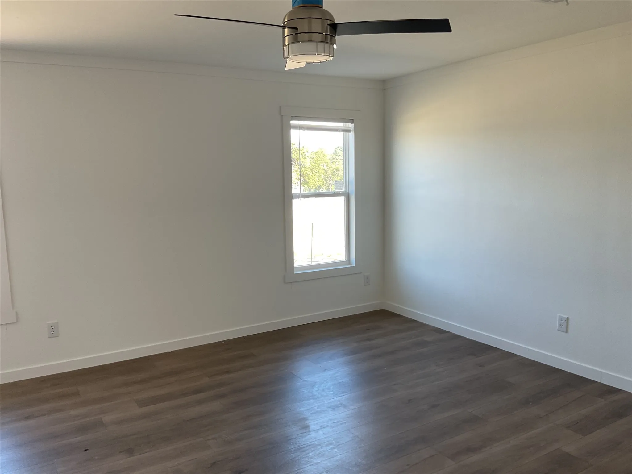 Room featuring wood-finish flooring, a single window with white trim, a ceiling fan with black blades and a brushed nickel housing, white walls, and white baseboards