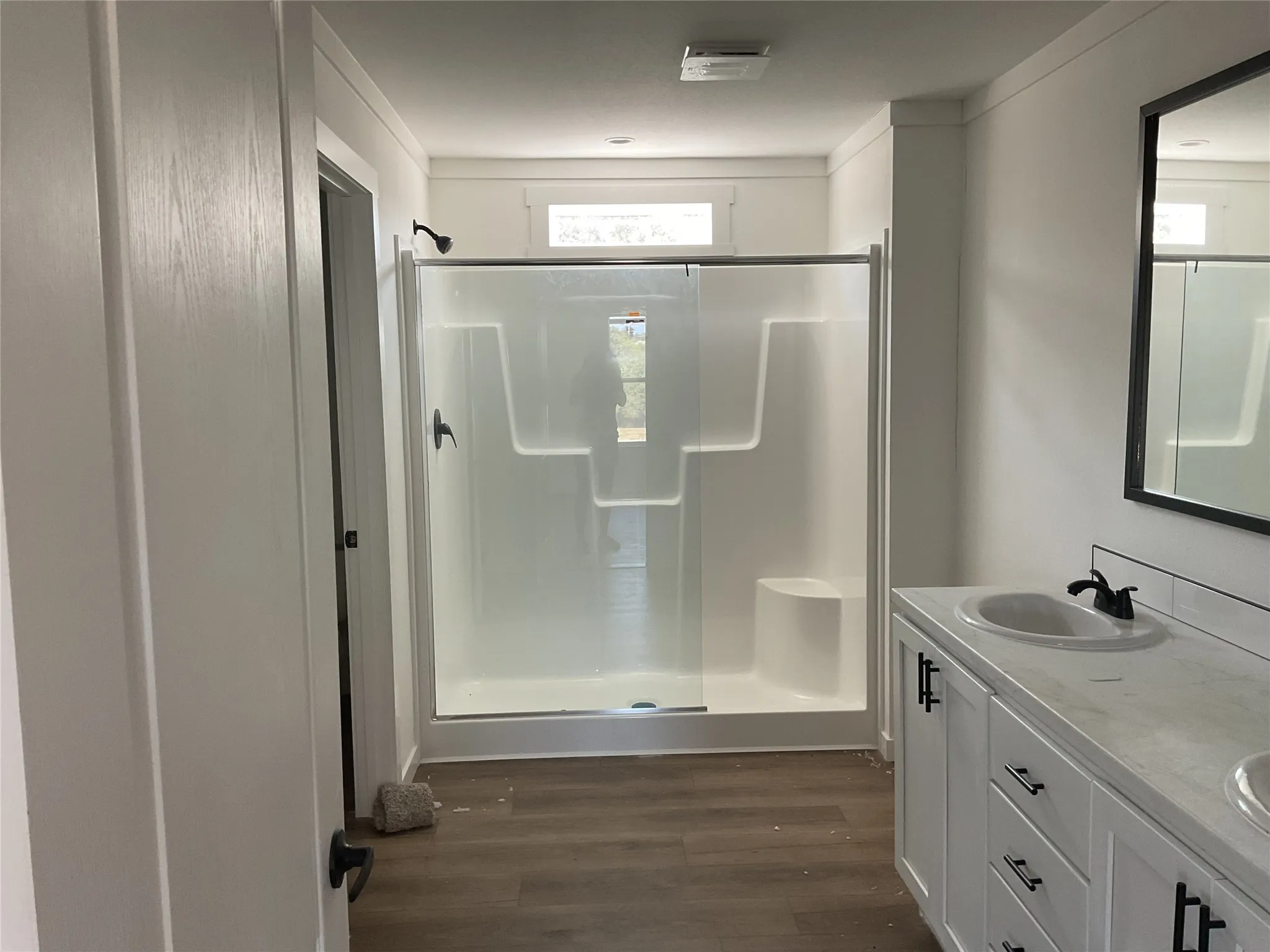 Dual basin vanity with matte black hardware, white cabinetry, wood-finish flooring, and a walk-in shower with a sliding glass door