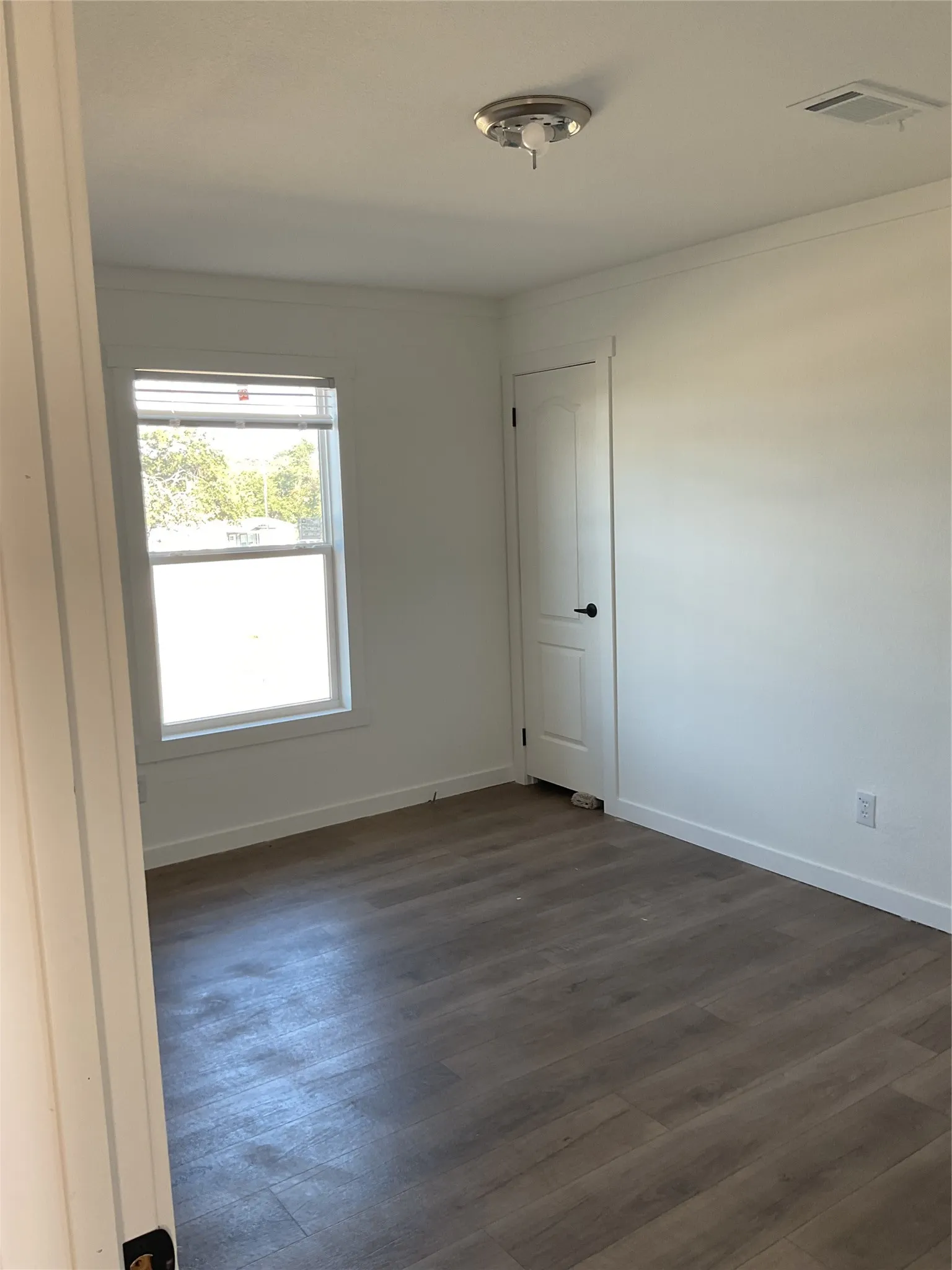 Room featuring wood-finish flooring, a white trim package, and a window with blinds