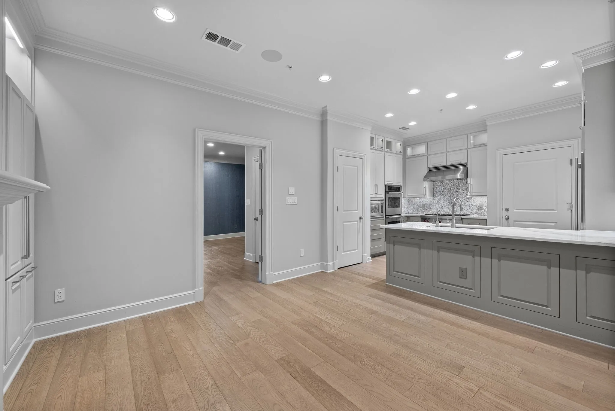 Open-concept kitchen featuring an oversized island with panel detailing, light wood-finish flooring, recessed lighting, and a built-in stainless steel oven and microwave