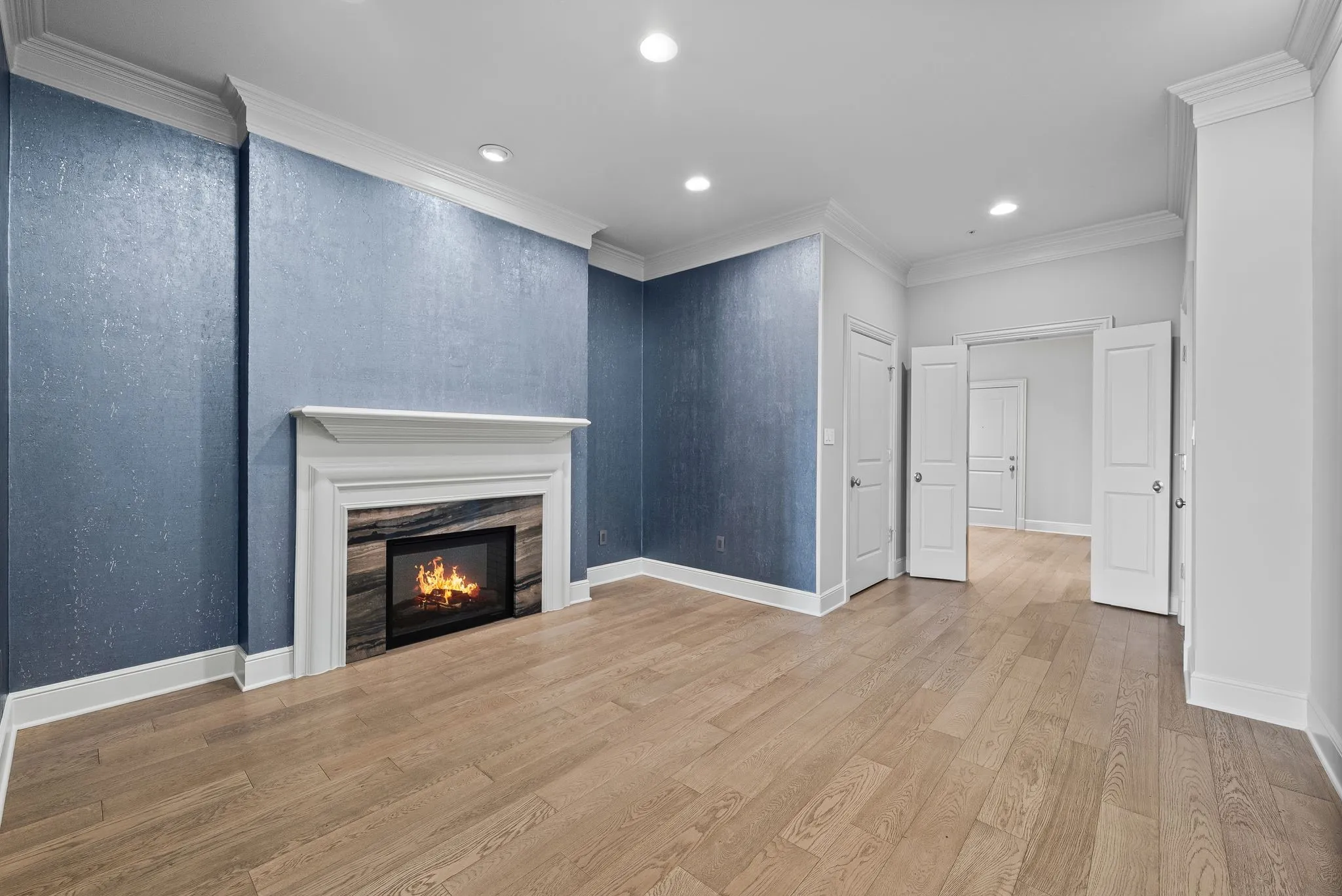 Spacious room featuring a fireplace with a white mantel and stone surround, wood-finish flooring, recessed lighting, and crown molding